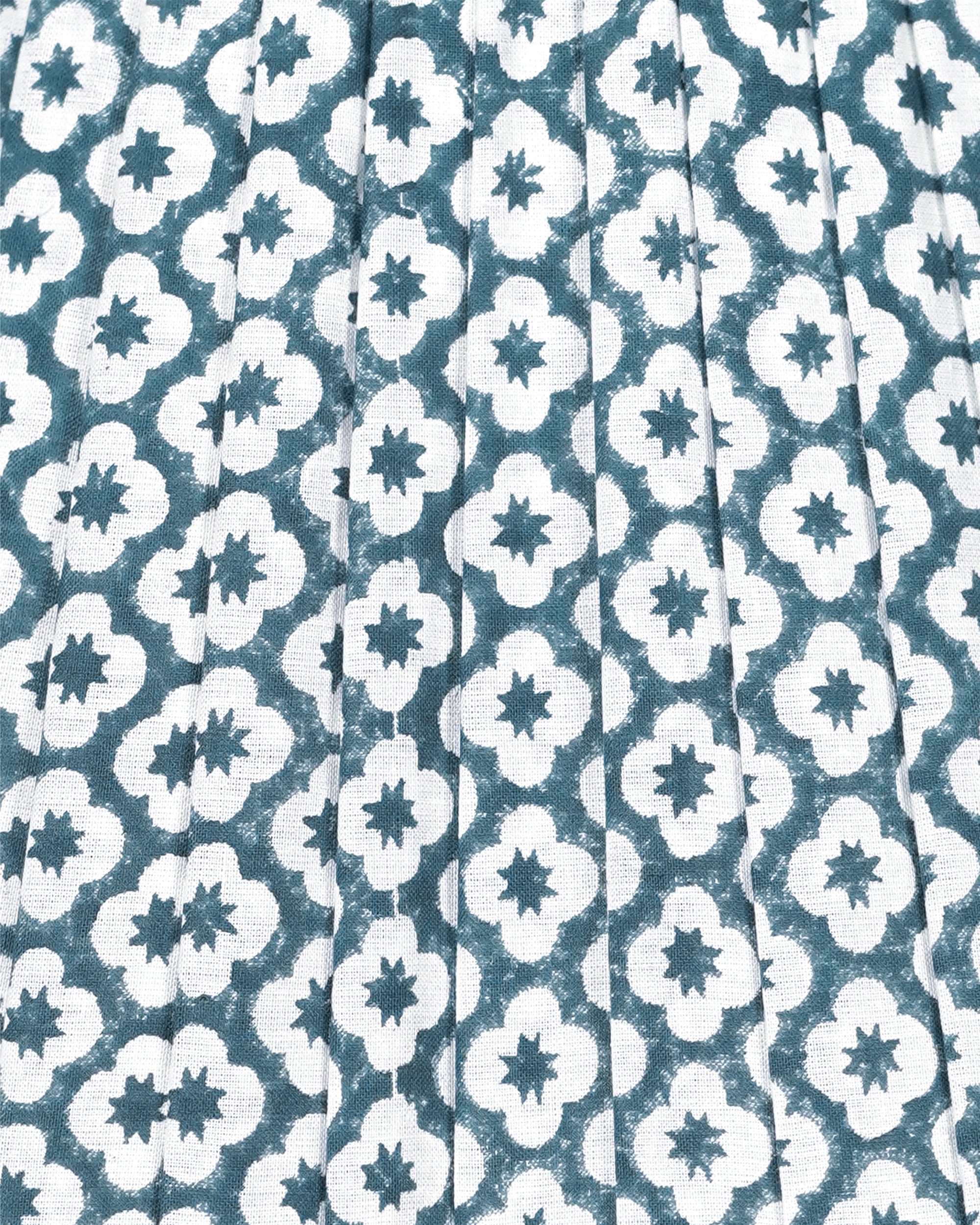 A close-up of a pleated fabric with a repeating white quatrefoil and star pattern on a muted teal blue background.