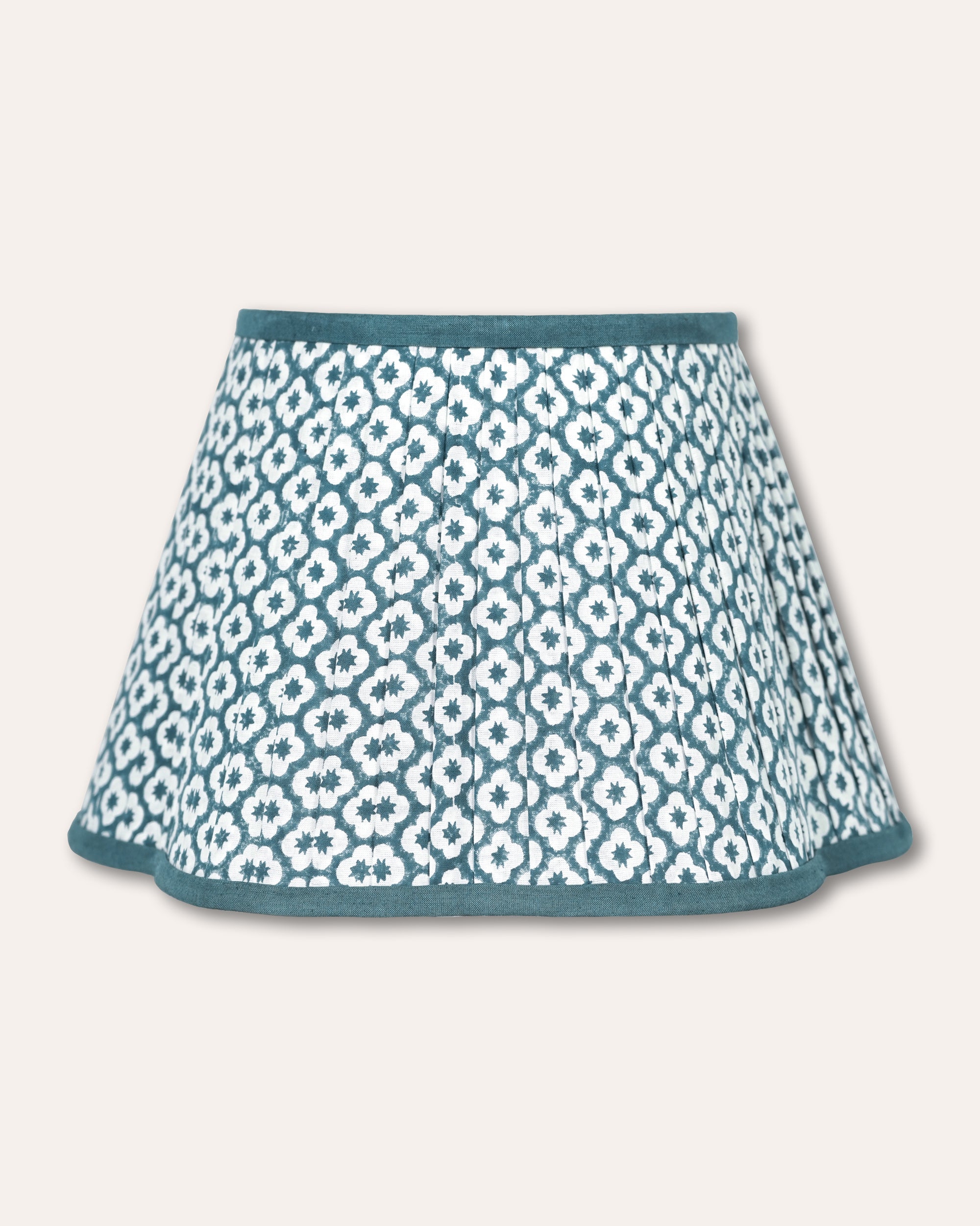 A pleated luxor lampshade with a teal and white geometric floral pattern, featuring solid teal trim at the waistband and hem, shown against a light beige background.