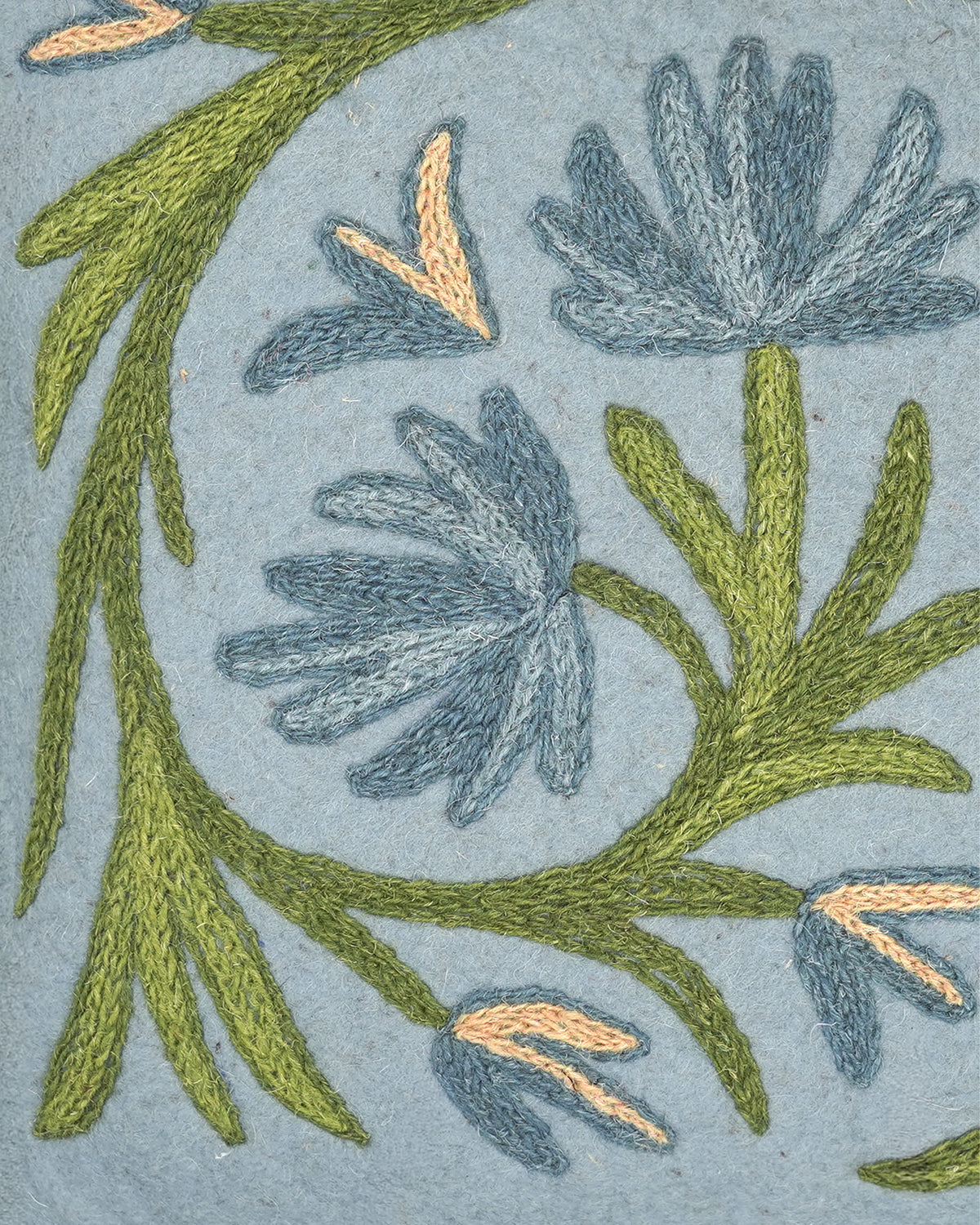 Close-up of a namda cushion featuring blue-grey flowers and olive green leaves stitched onto a light blue-grey fabric background.