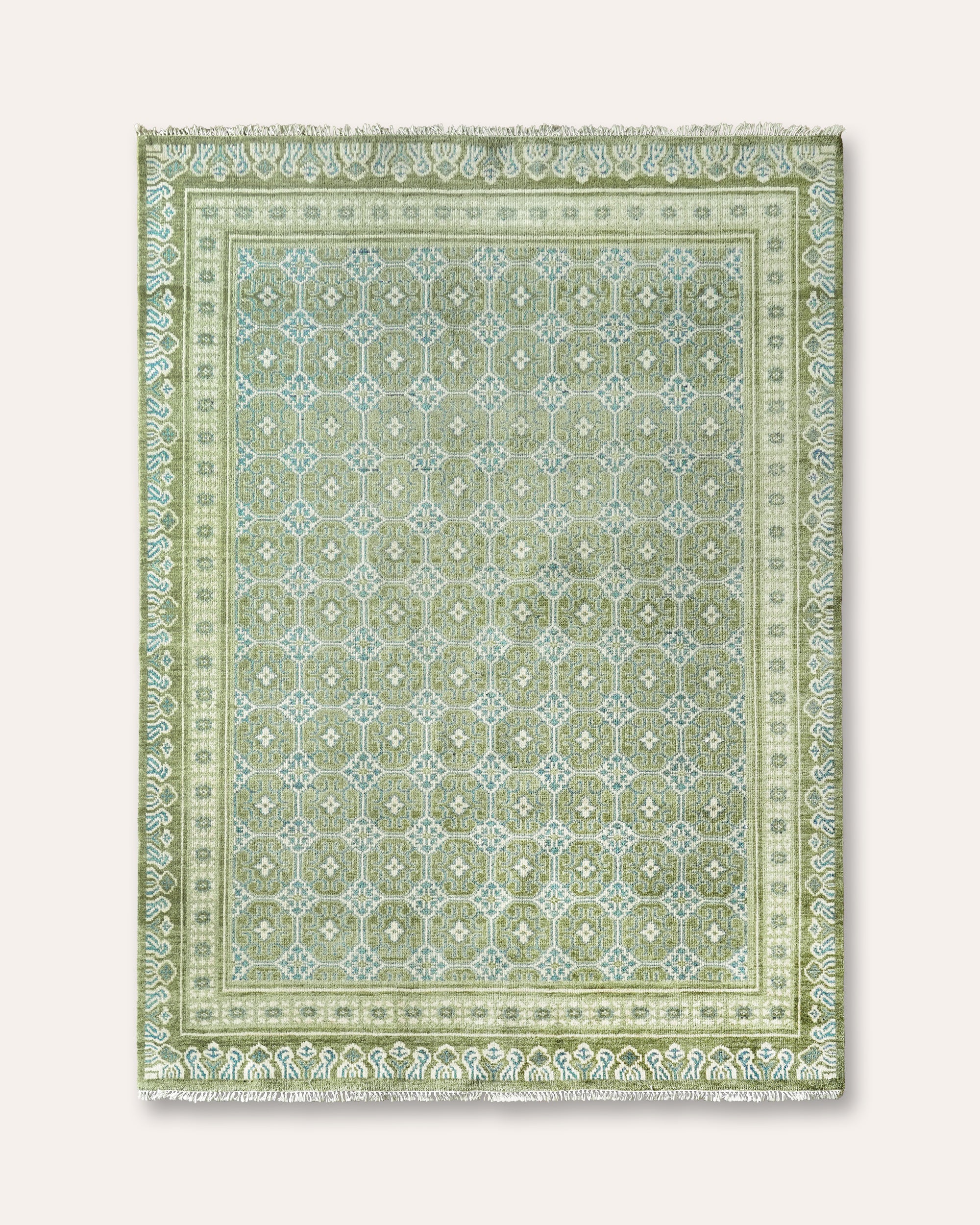 A rectangular area rug with a traditional geometric pattern in shades of sage green, light green, and cream, featuring a fringed edge.