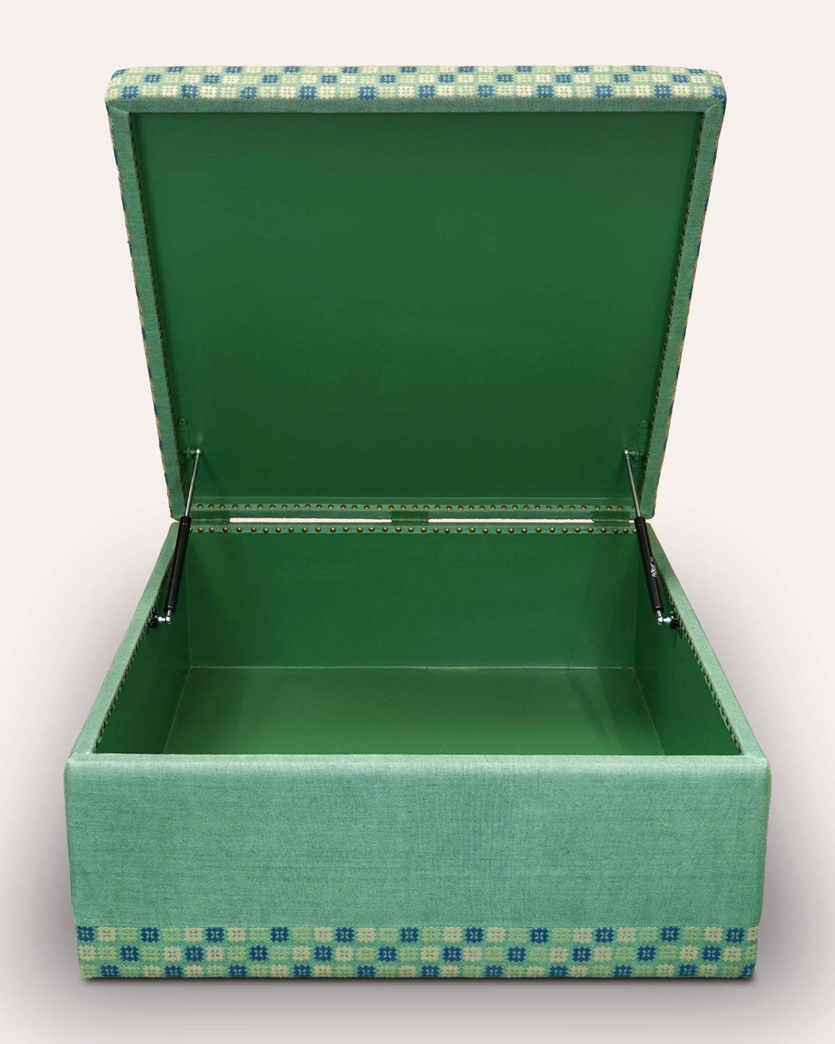 An open upholstered storage box with a green interior and a green, blue, and beige patterned fabric exterior, shown on a light gray background.