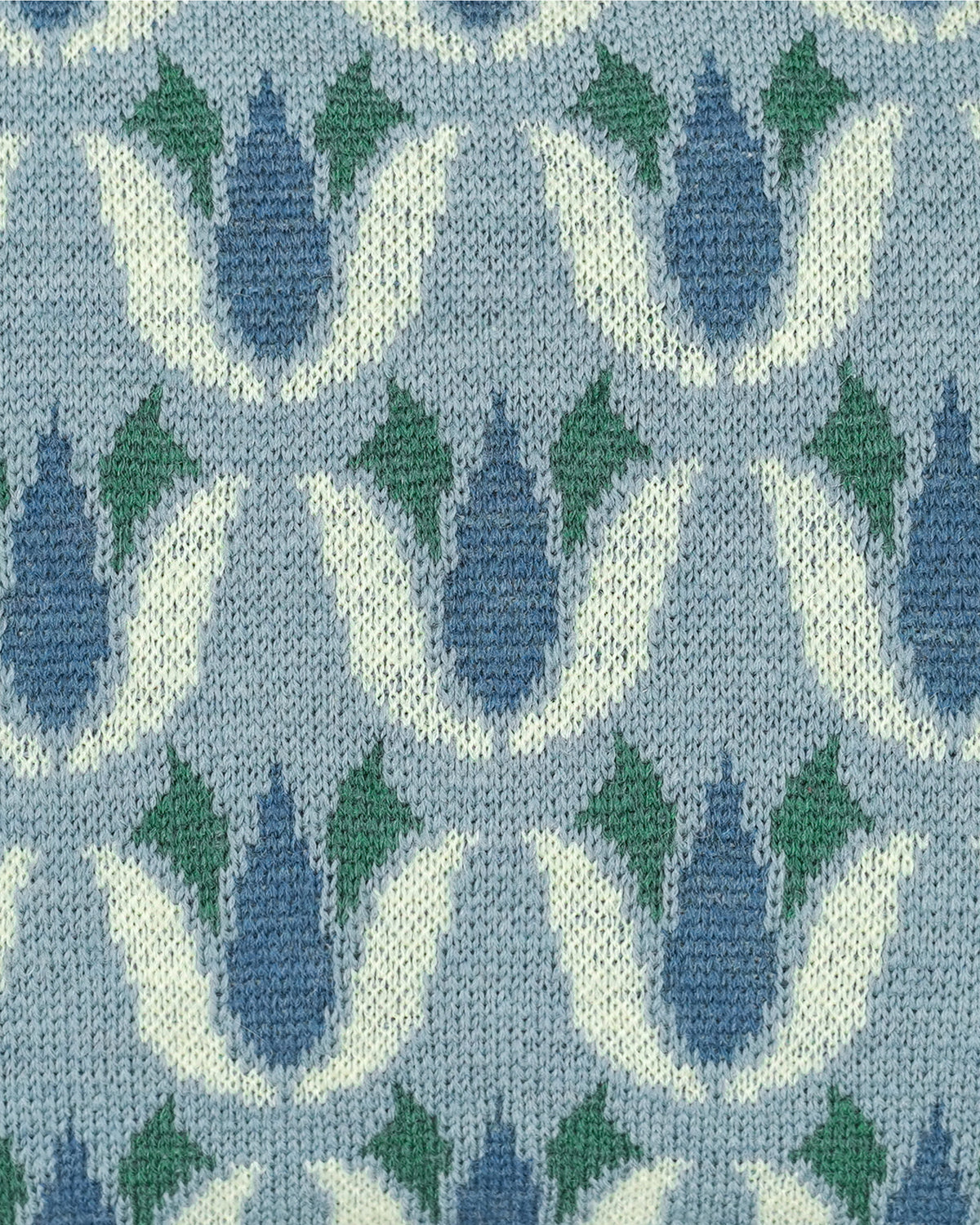 Close-up of a knitted fabric with a repeating tulip-like pattern in light blue, muted blue, green, and off-white.