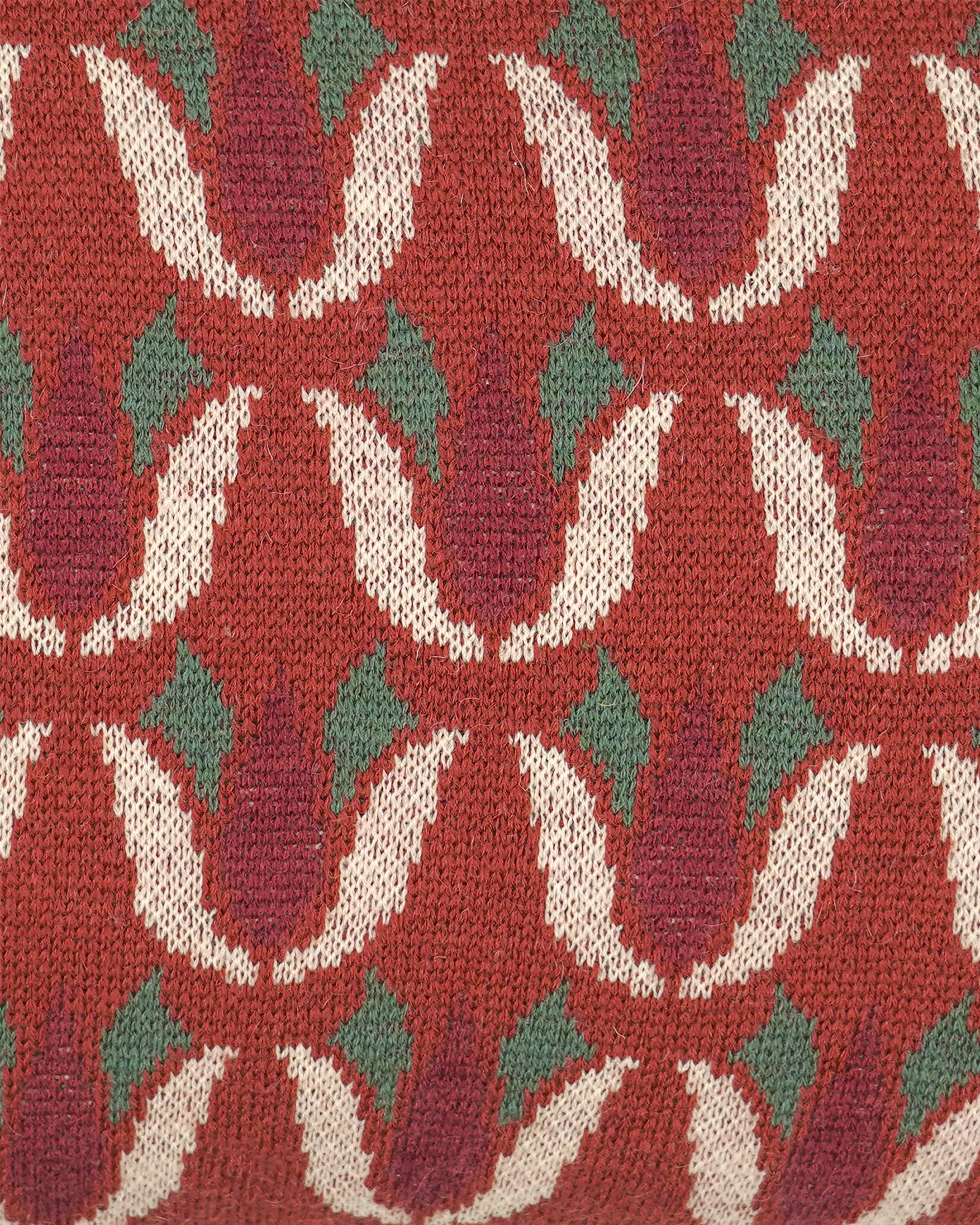 Close-up of a knitted textile with a repeating floral pattern in rust red, cream, and muted green.