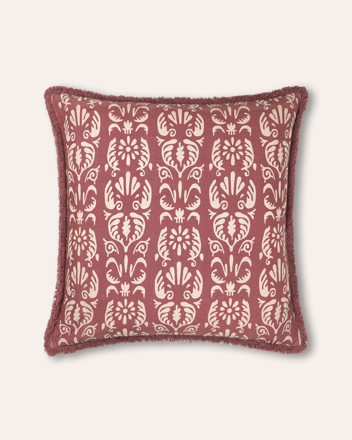 A decorative square cushion with a dusty rose and cream damask pattern, featuring a fringed edge, shown against a light beige background.