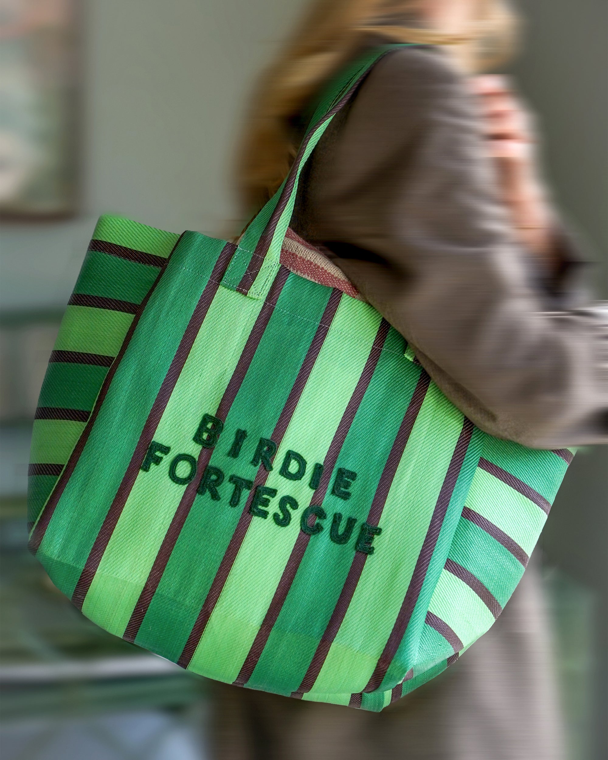 Green striped tote bag with 'Birdie Fortescue' branding held by a person.