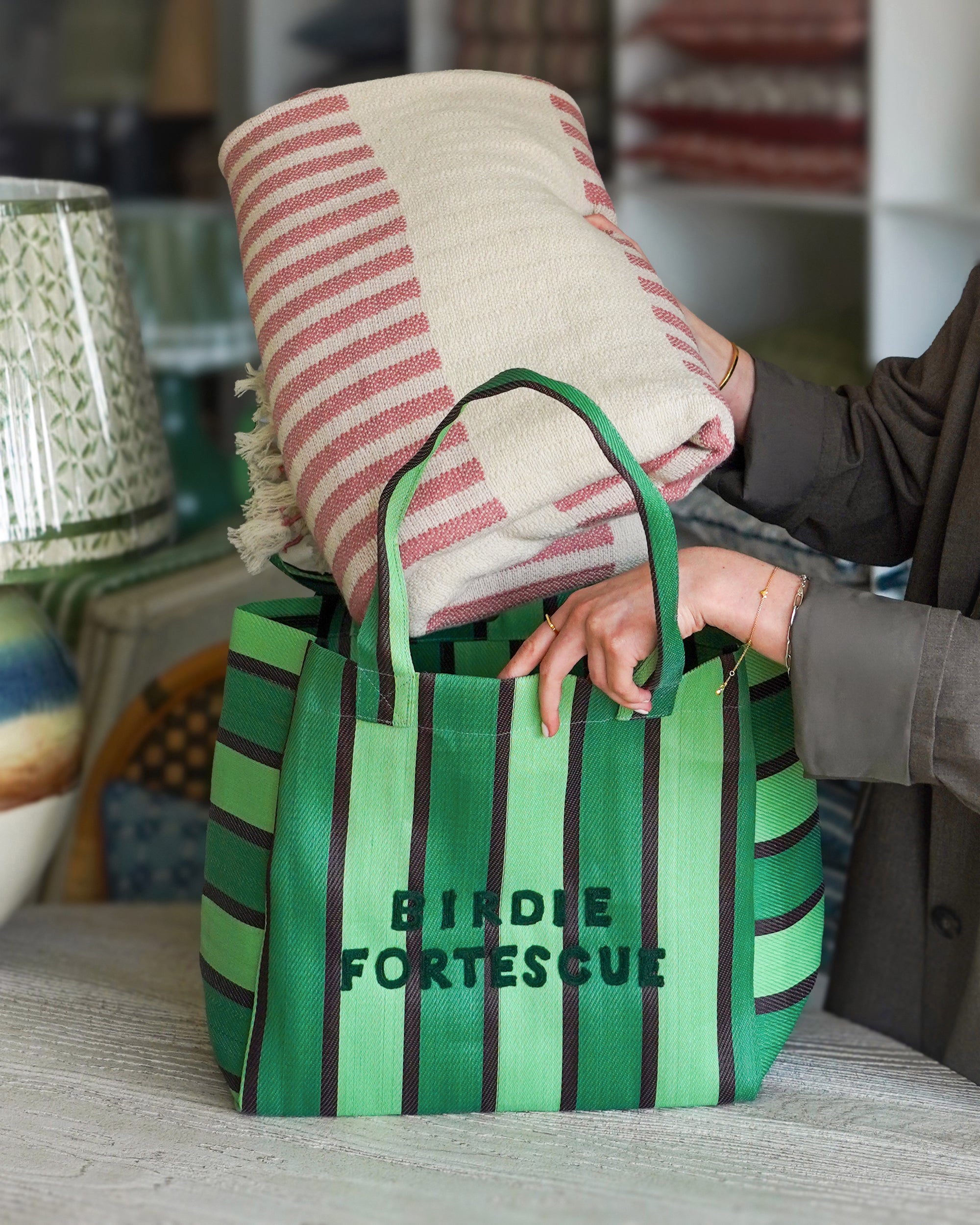 Green striped tote bag with 'Birdie Fortescue' branding, holding a folded blanket.