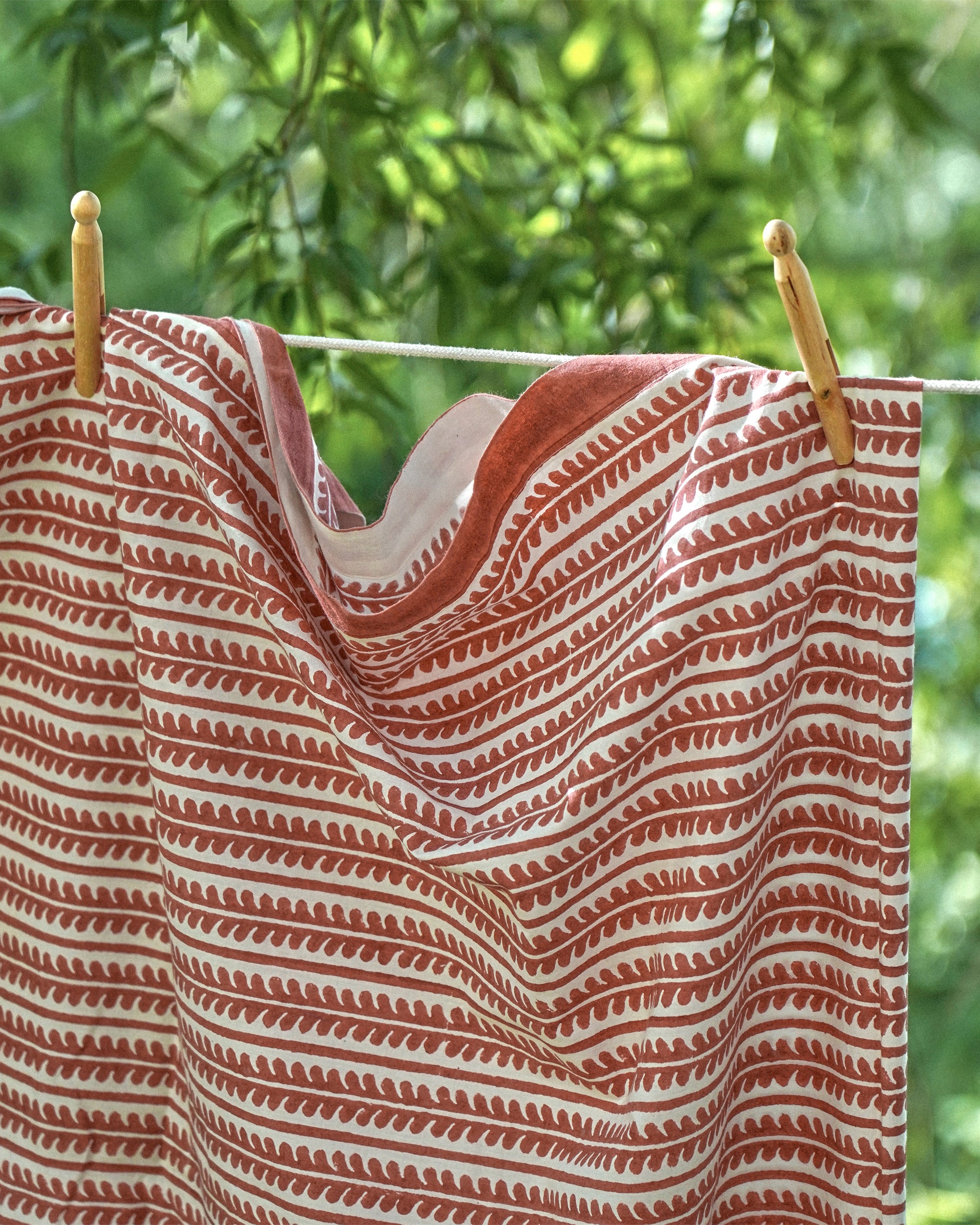 Red and white striped tablecloth hanging on a clothesline with greenery in the background