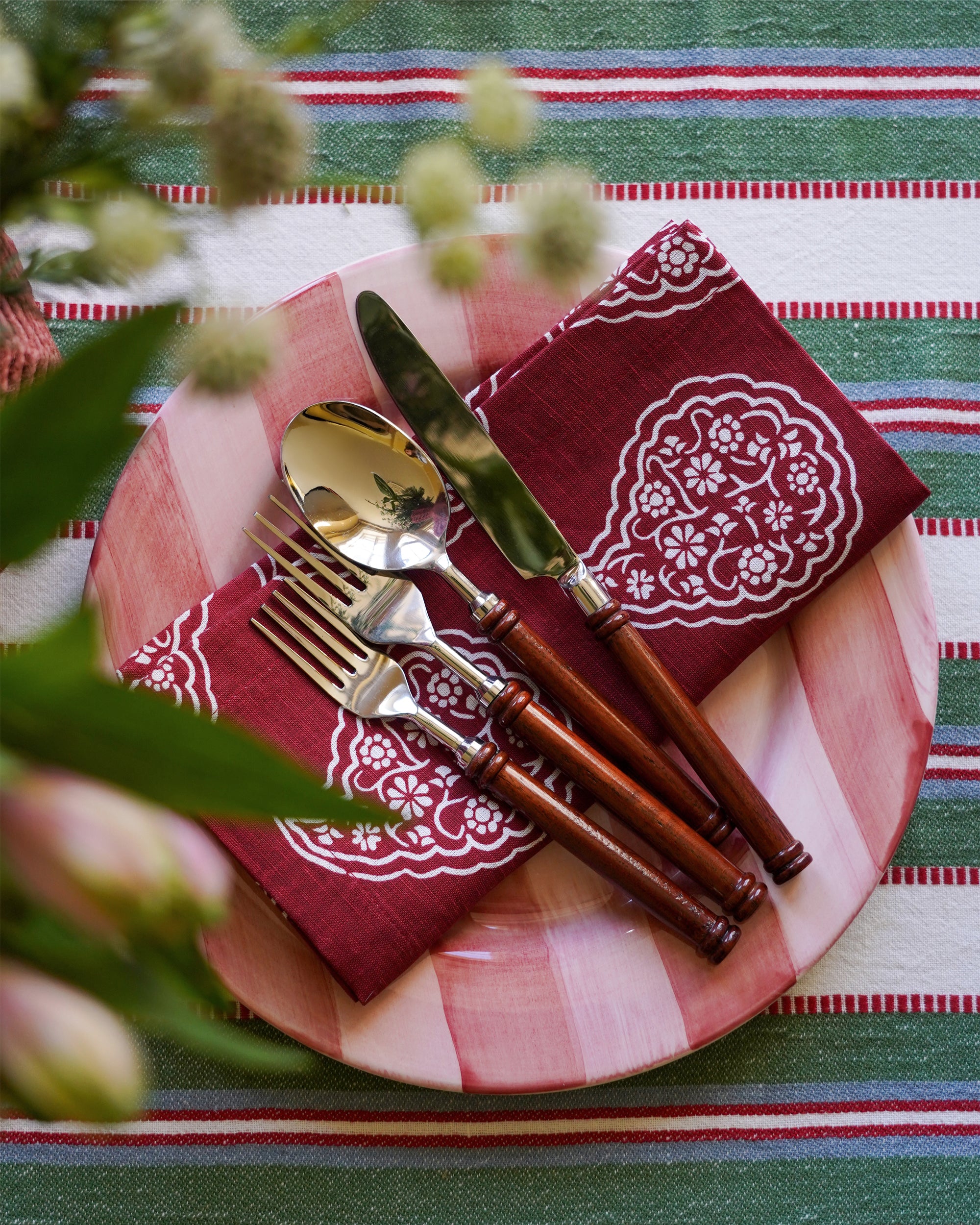 Plated setting with red patterned napkins, silverware, and a striped tablecloth.