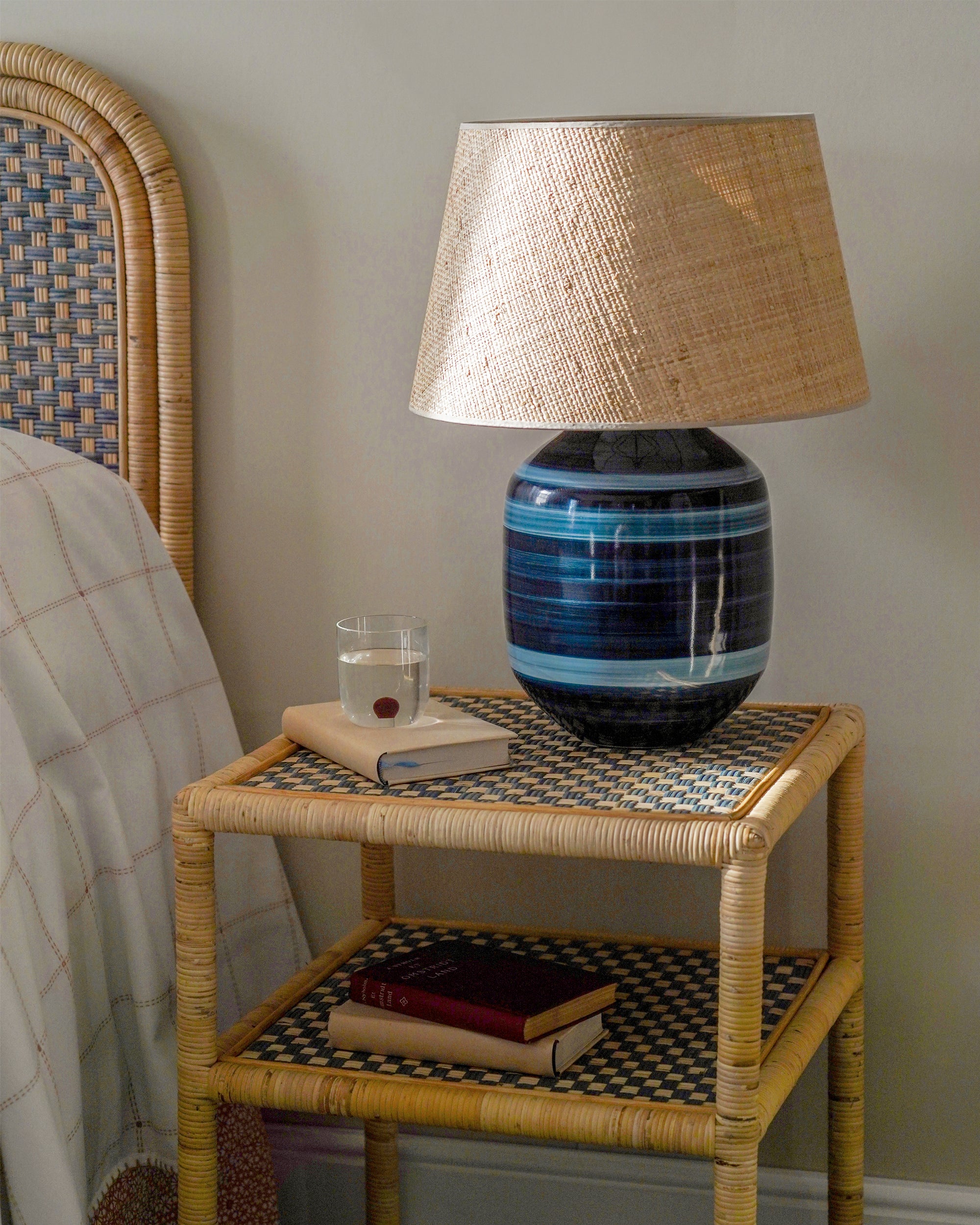 Napoleon Chao table lamp on a wicker side table with books and a glass of water.