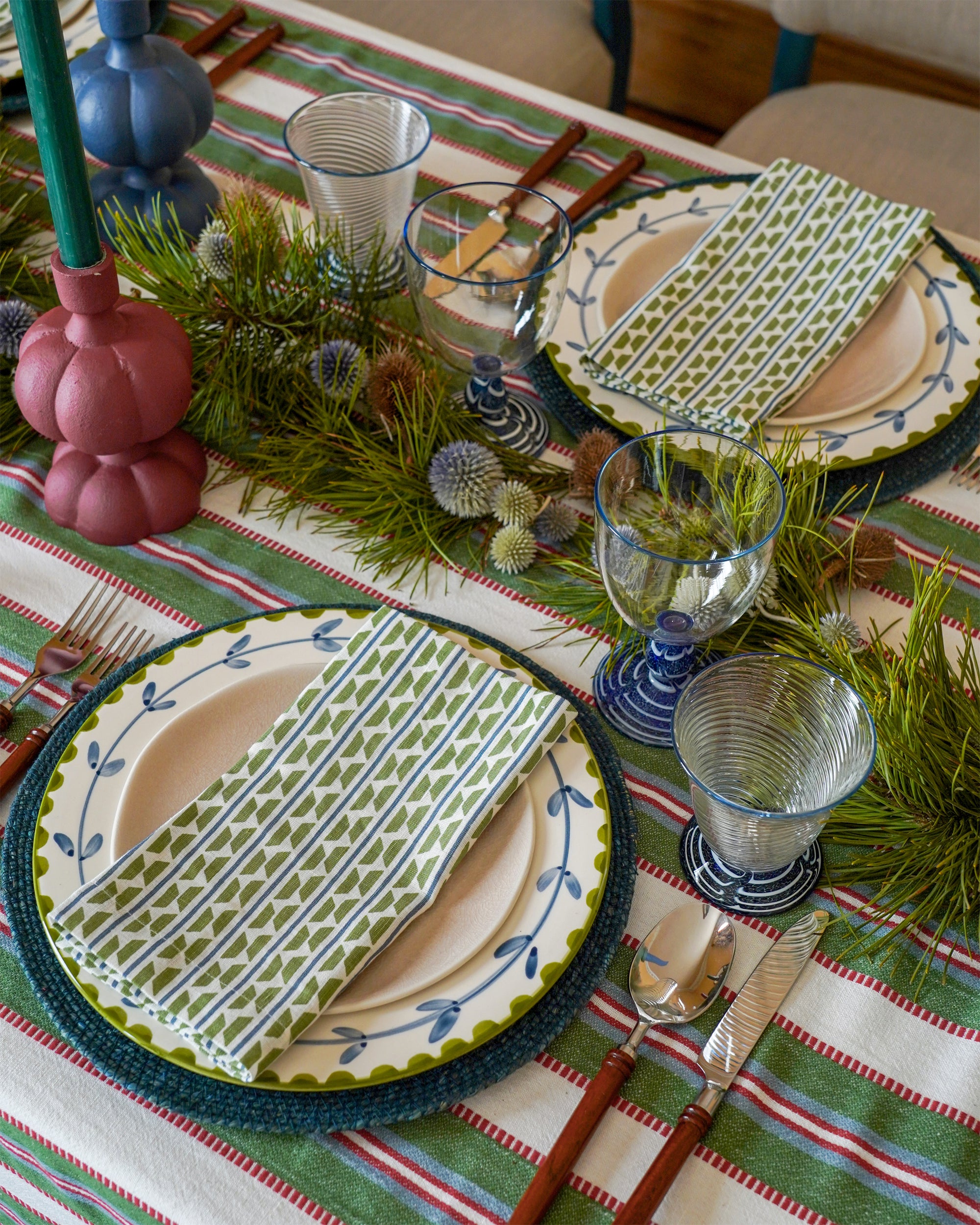 Decorative table setting with patterned plates, glasses, and cutlery on a striped tablecloth.