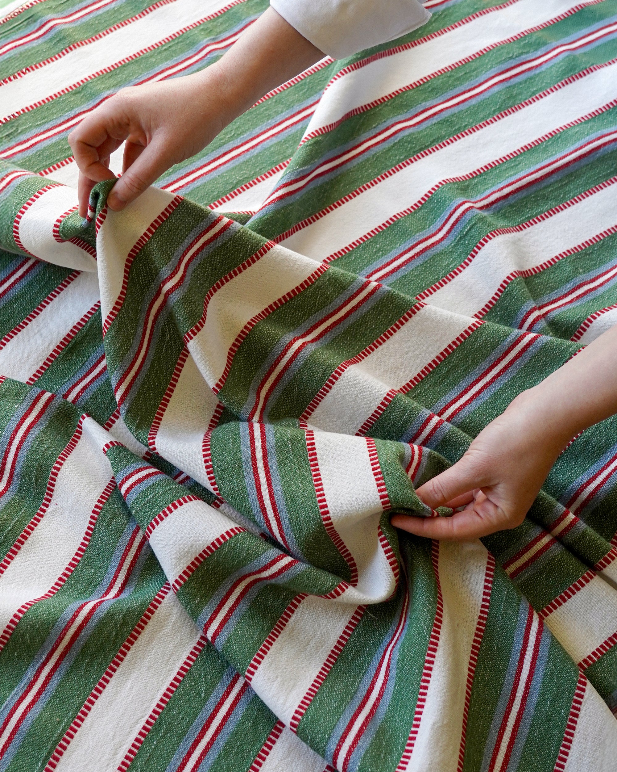 Green, red, and white striped fabric being handled by a person.