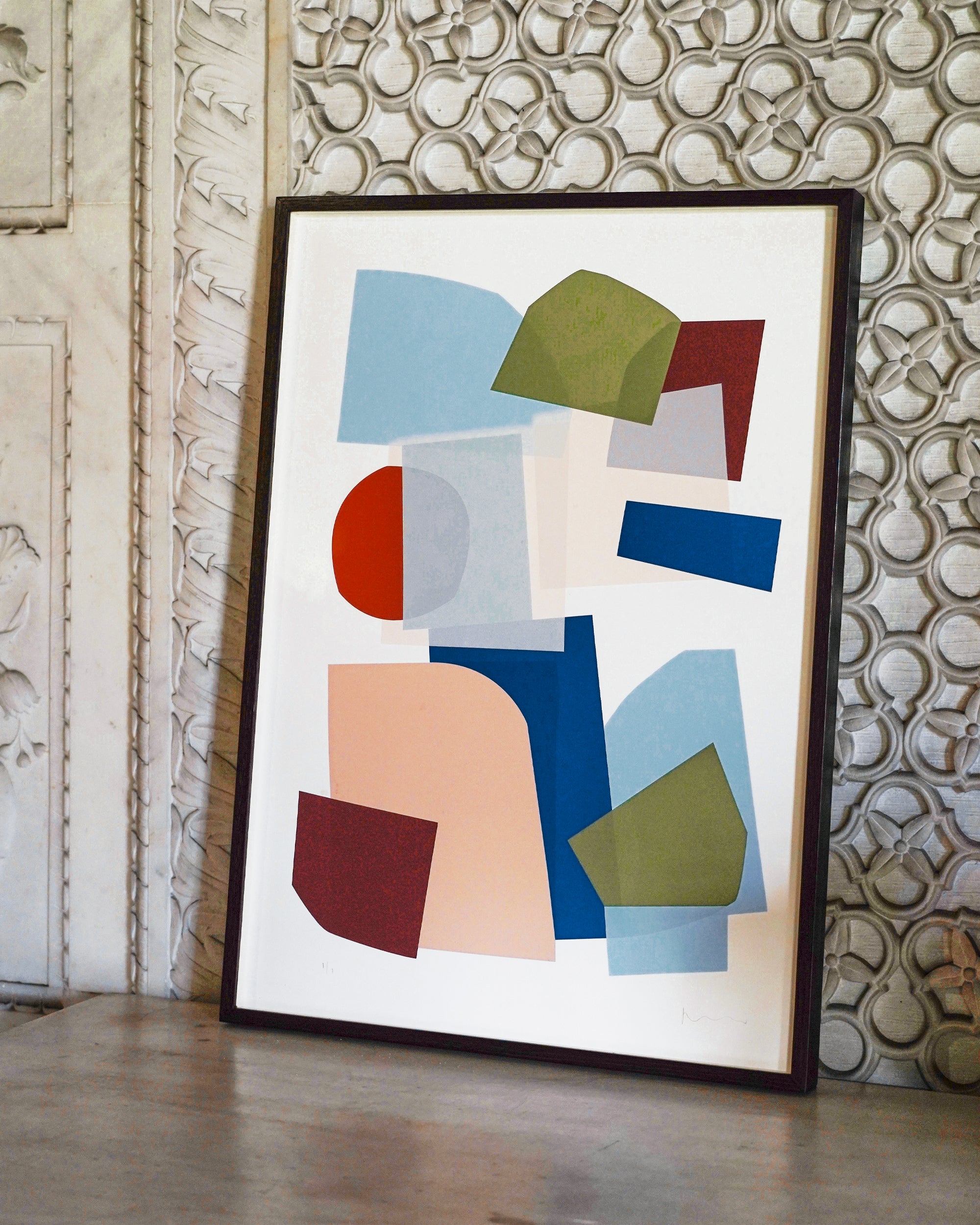 Framed abstract art piece with geometric shapes on a textured wall.