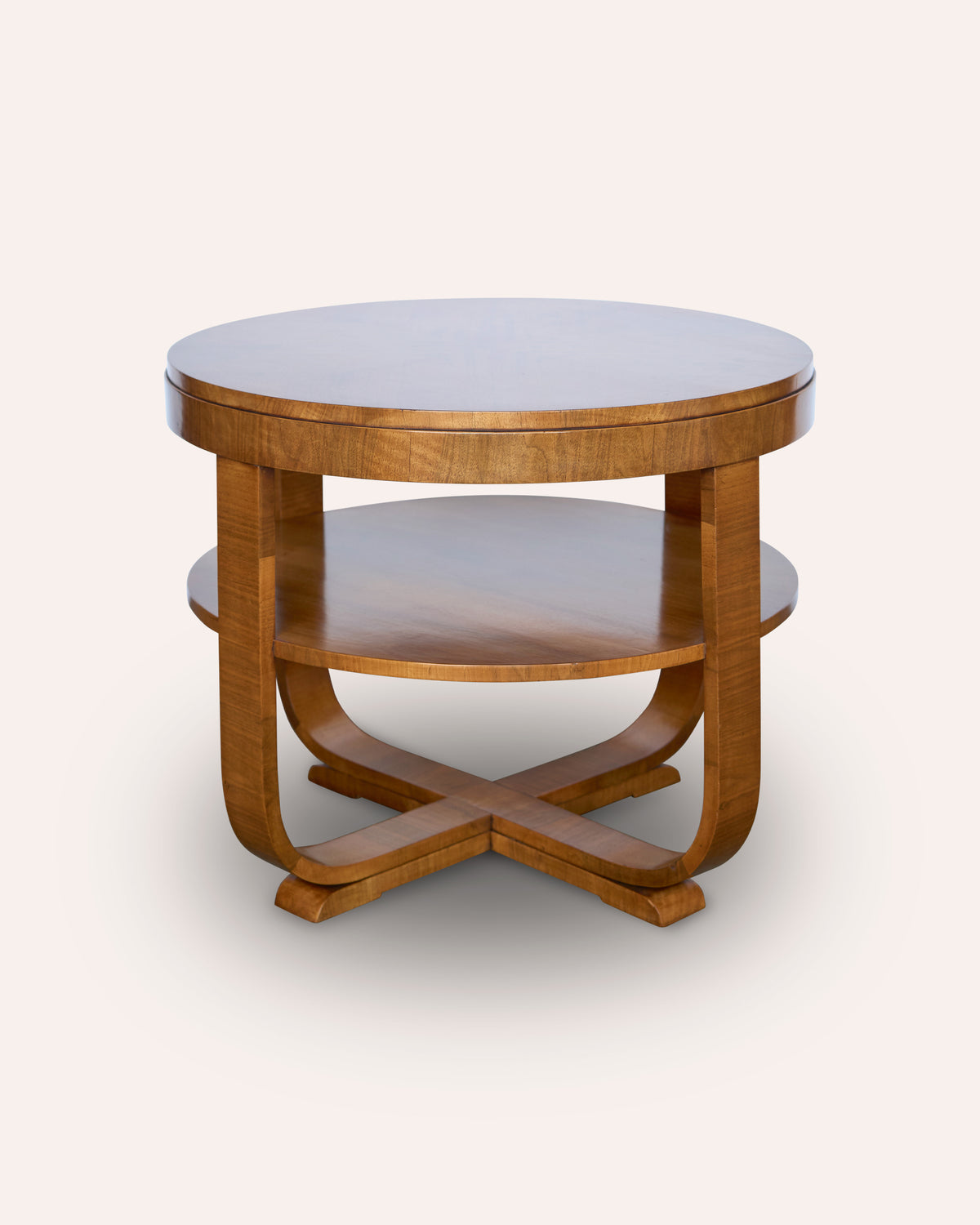 A mid-century modern round wooden side table with a top surface, a lower shelf, and a curved cross-shaped base, shown against a plain off-white background.