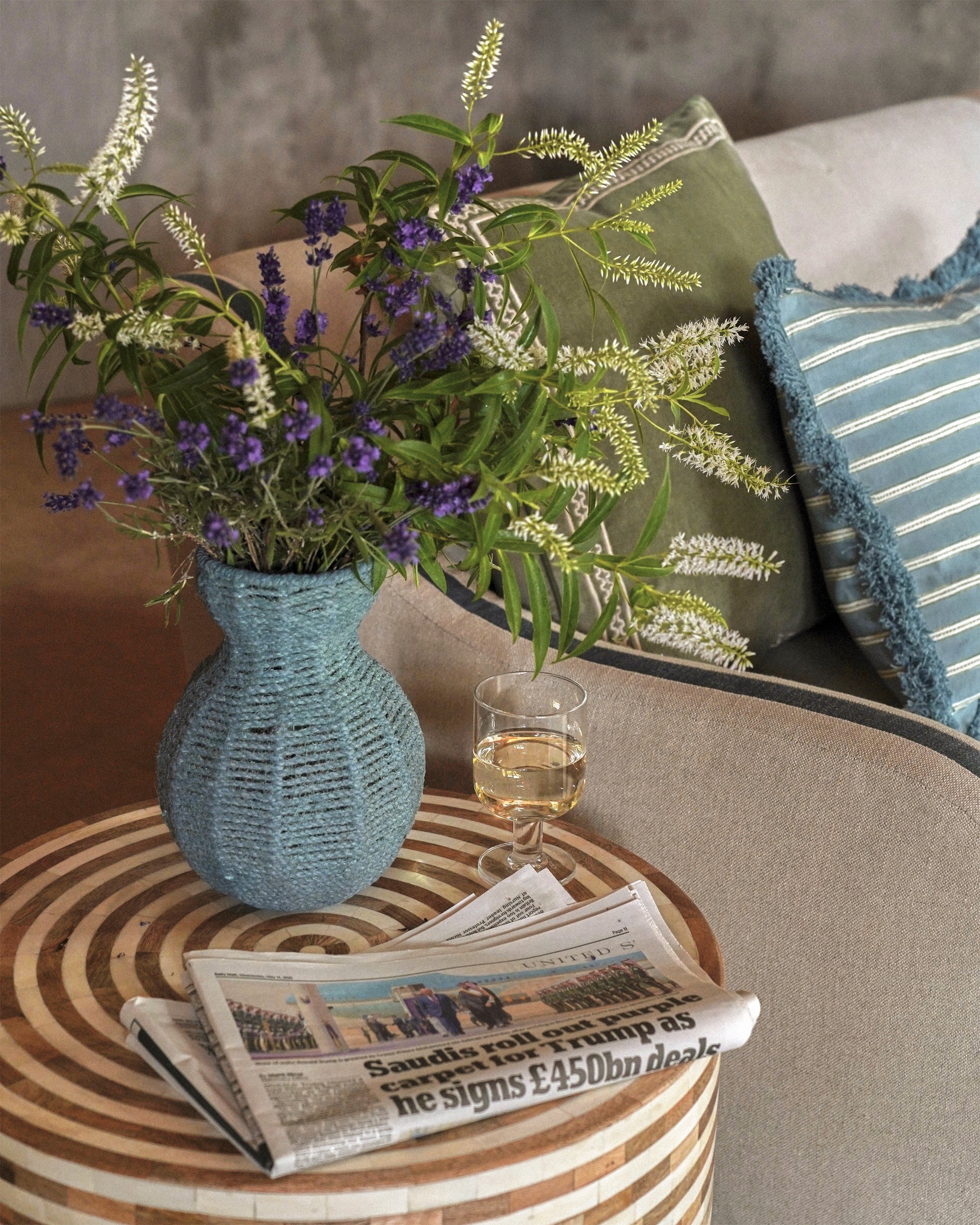 Decorative vase with flowers on a round wooden table next to a sofa with cushions.