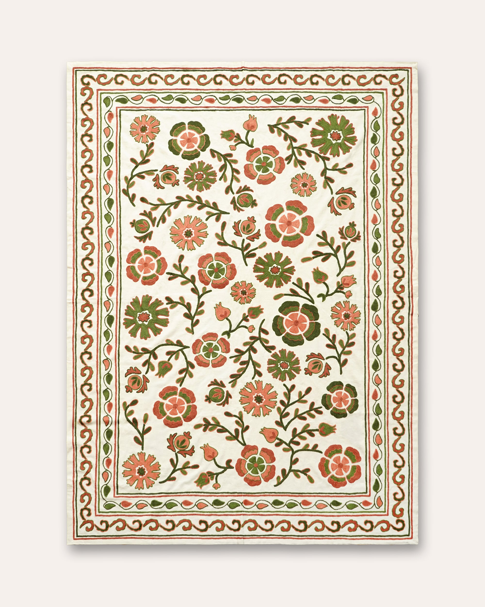 A rectangular embroidered suzani throw with an intricate floral pattern in muted green, terracotta, and coral, framed by a decorative border, shown against a light beige background.