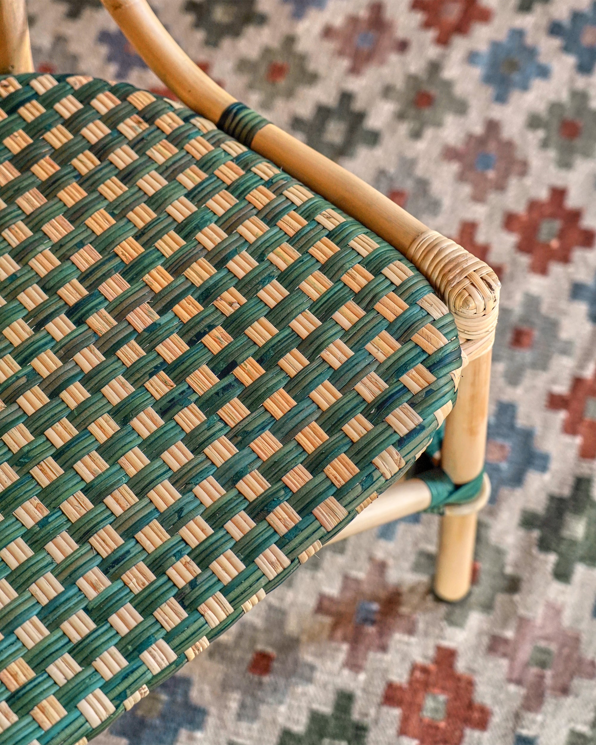 Woven chair with green and beige pattern on a multicolored floral rug
