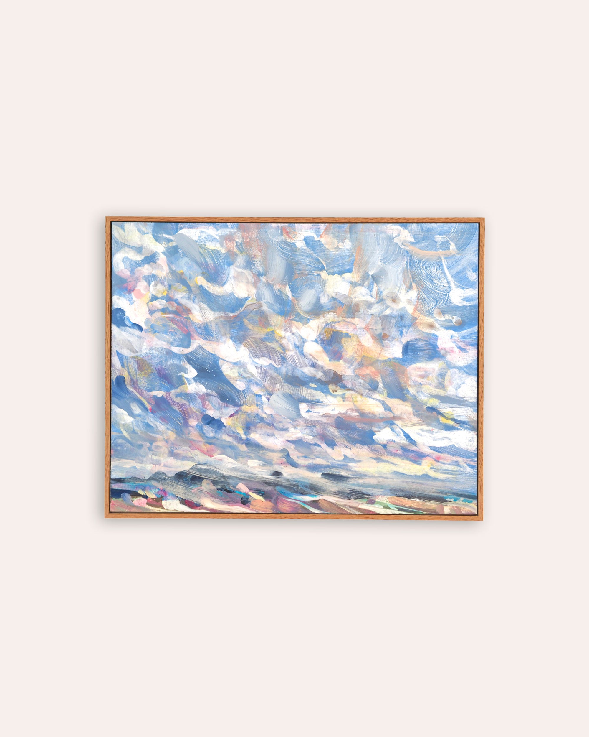 An abstract landscape painting of a cloudy sky with blue, white, and soft peach tones, housed in a light natural wood frame and displayed on a warm off-white wall.