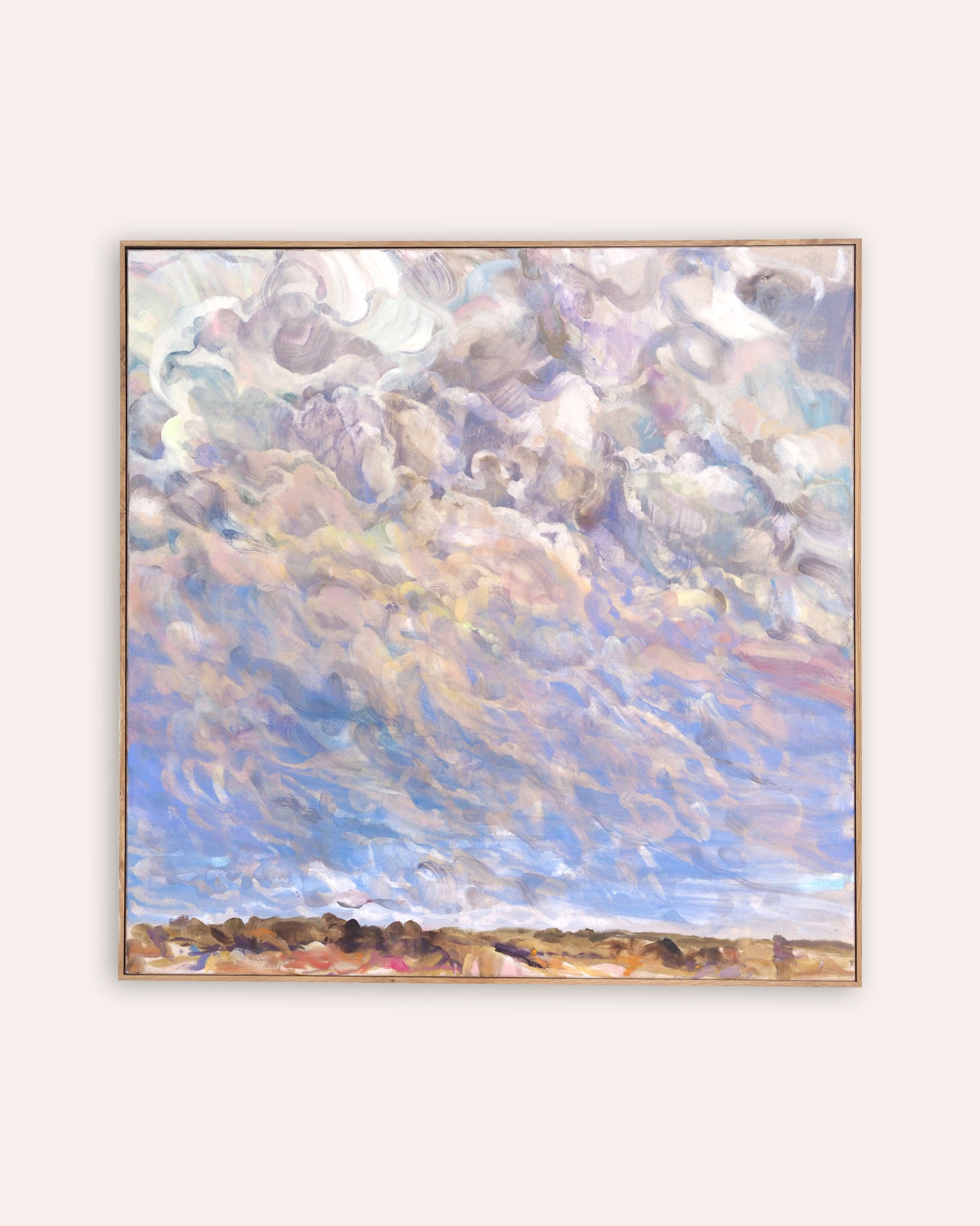 A framed landscape painting featuring a dramatic, textured sky with swirling clouds in shades of blue, purple, grey, and cream, above a low, dark shoreline. The painting is housed in a thin, light wood frame and is displayed against a solid, warm off-white background.