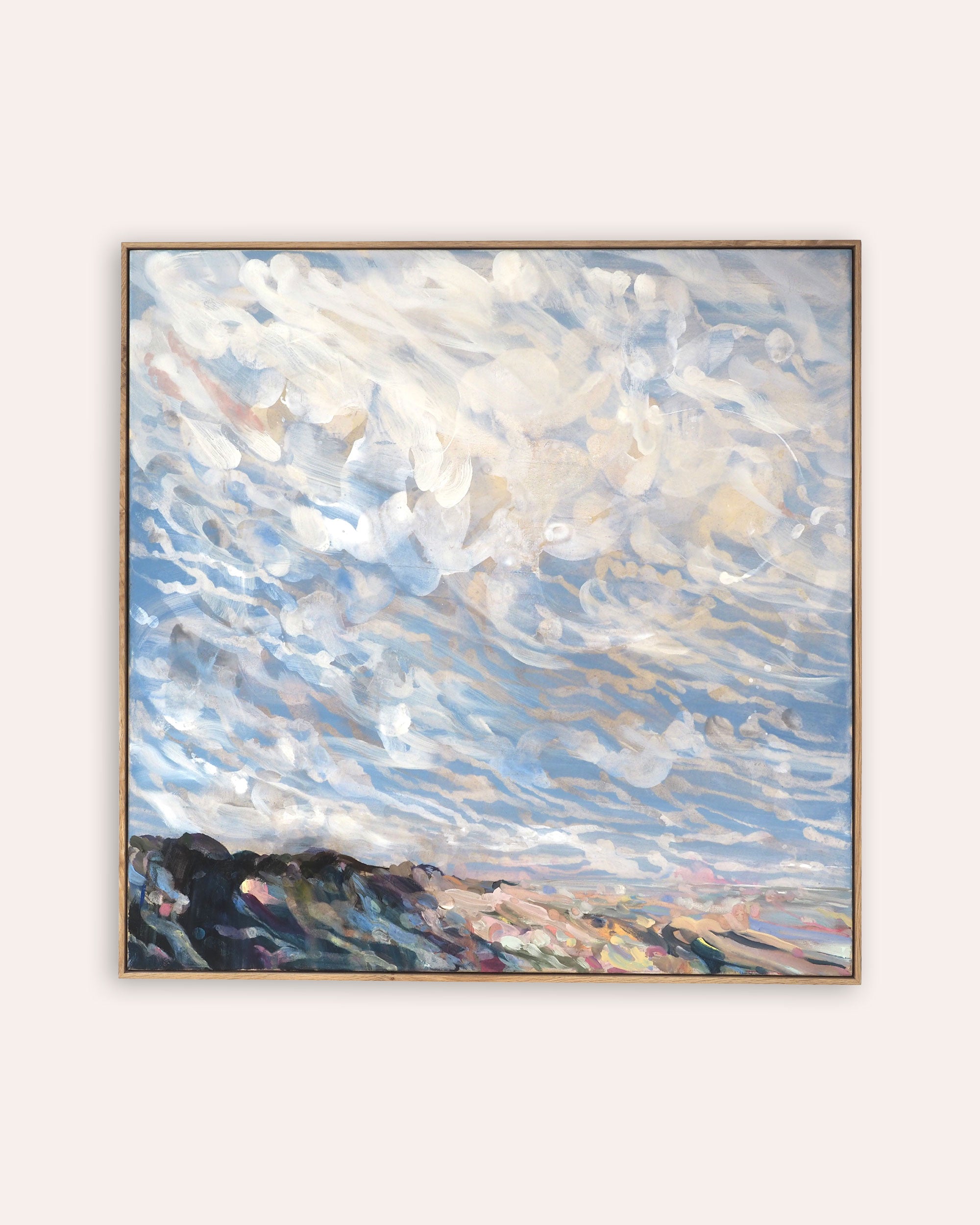 A framed landscape painting featuring a dramatic sky with swirling white and blue clouds, with dark, textured hills in the foreground, displayed on a light beige wall.
