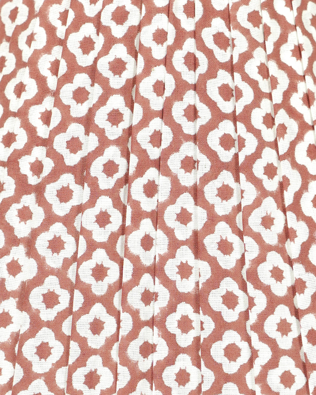 A close-up of a pleated fabric with a repeating white ikat-style geometric pattern on a muted terracotta or dusty rose background.