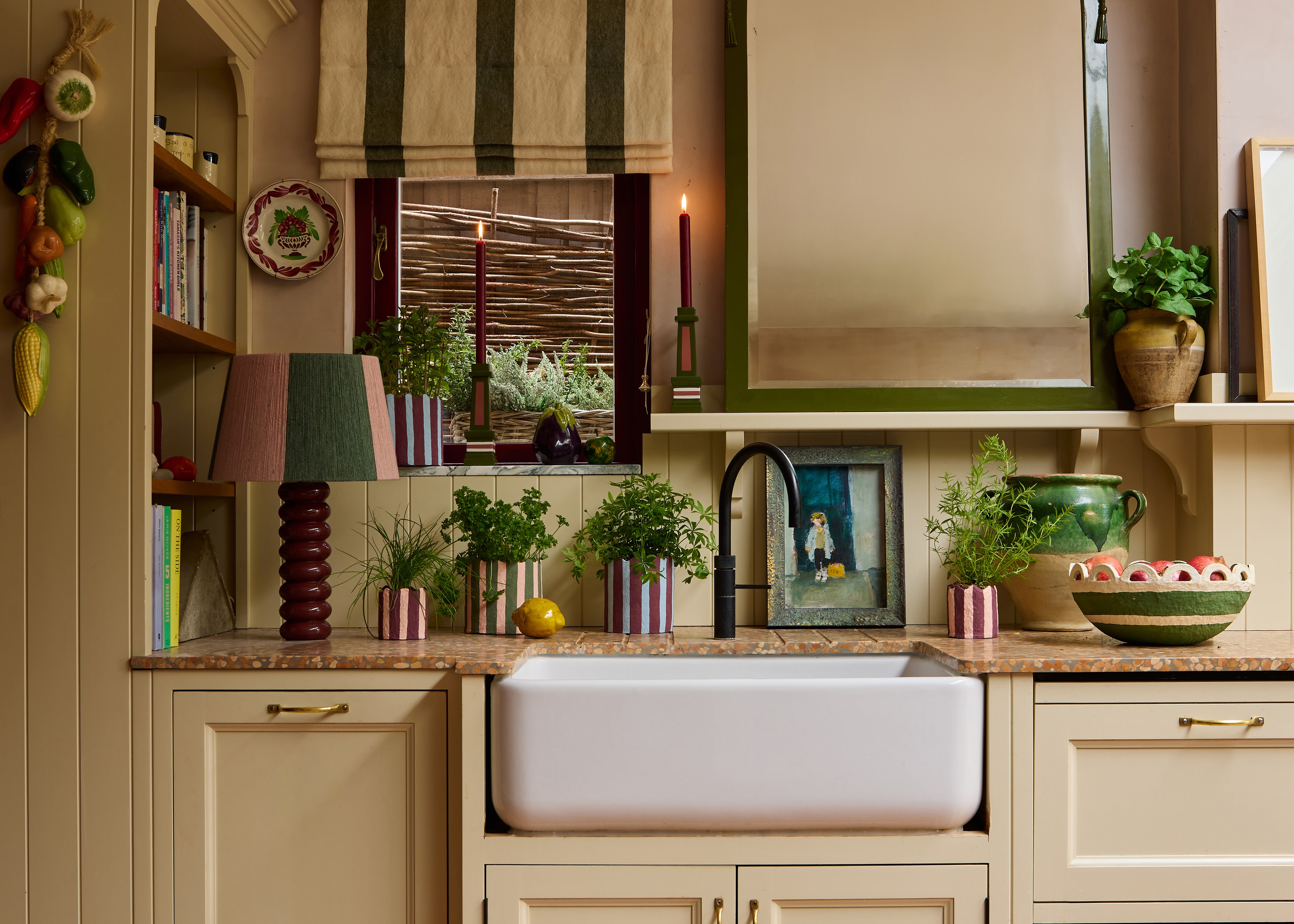 a landscape shot of a kitchen counter with a sink and window, decorated with lit candles in grown up candlesticks and must have planters