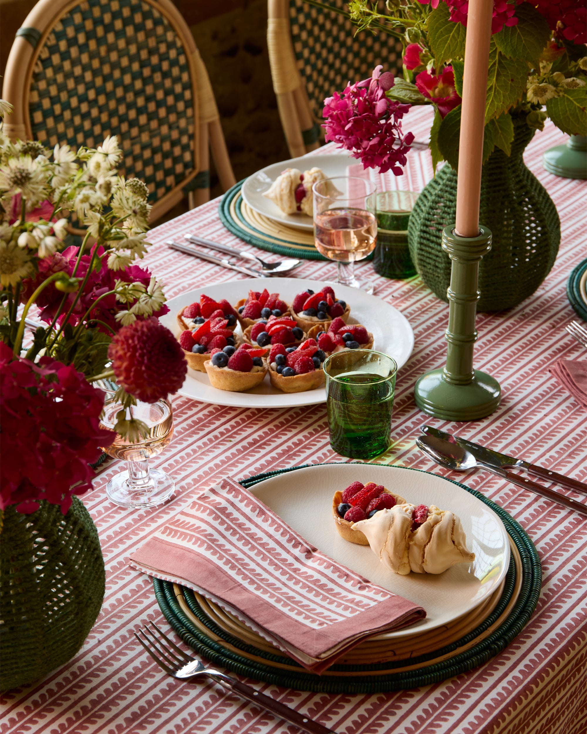 Elegant dining table setting with fruit tartlets, flowers, and patterned tablecloth.