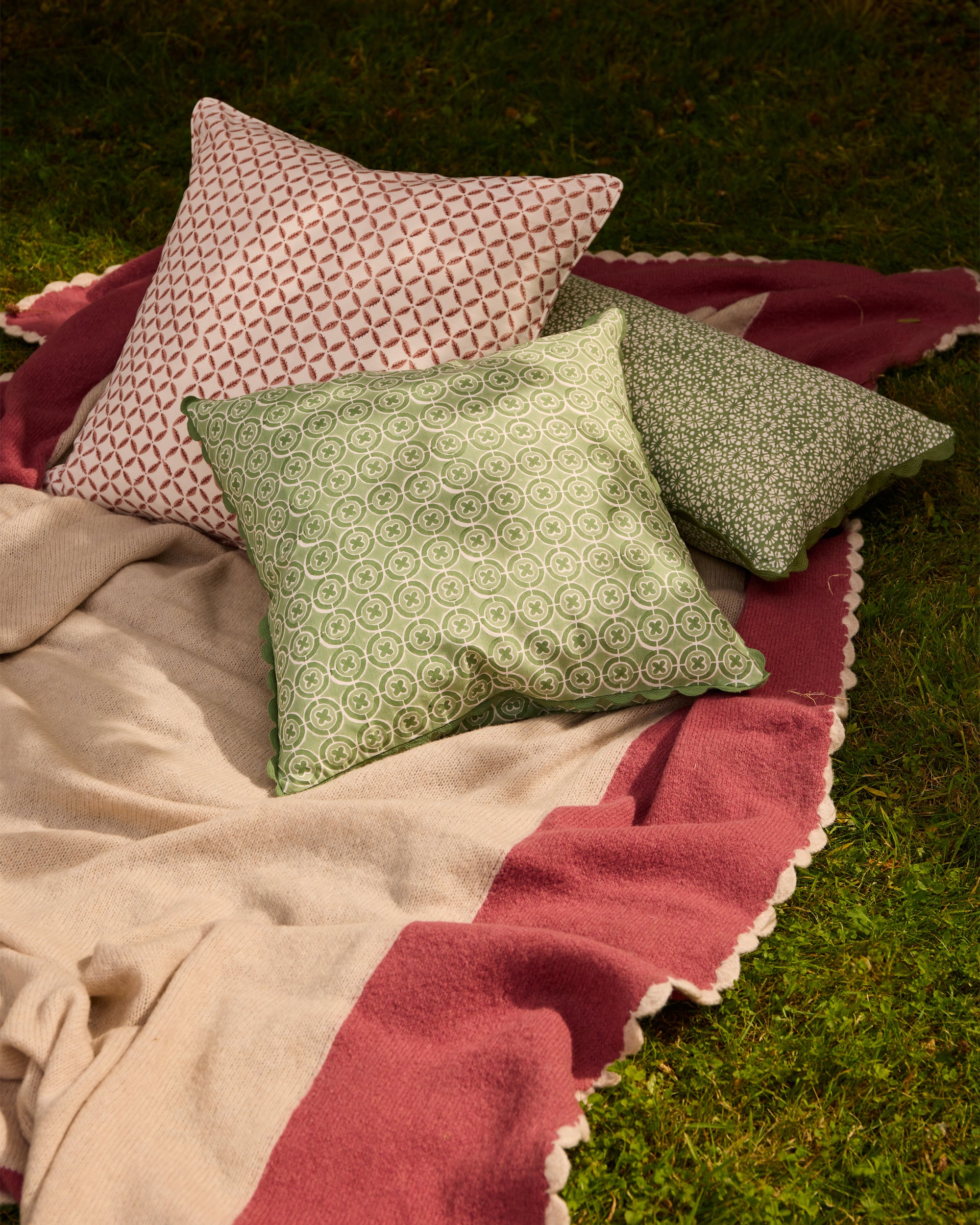 Summer outdoor garden lifestyle image featuring the Pink Bordered throw, Arriate Block Print Outdoor Cushion, green Ciculo Block Print Cushion and green Margarita Block Printed Bolster Cushion