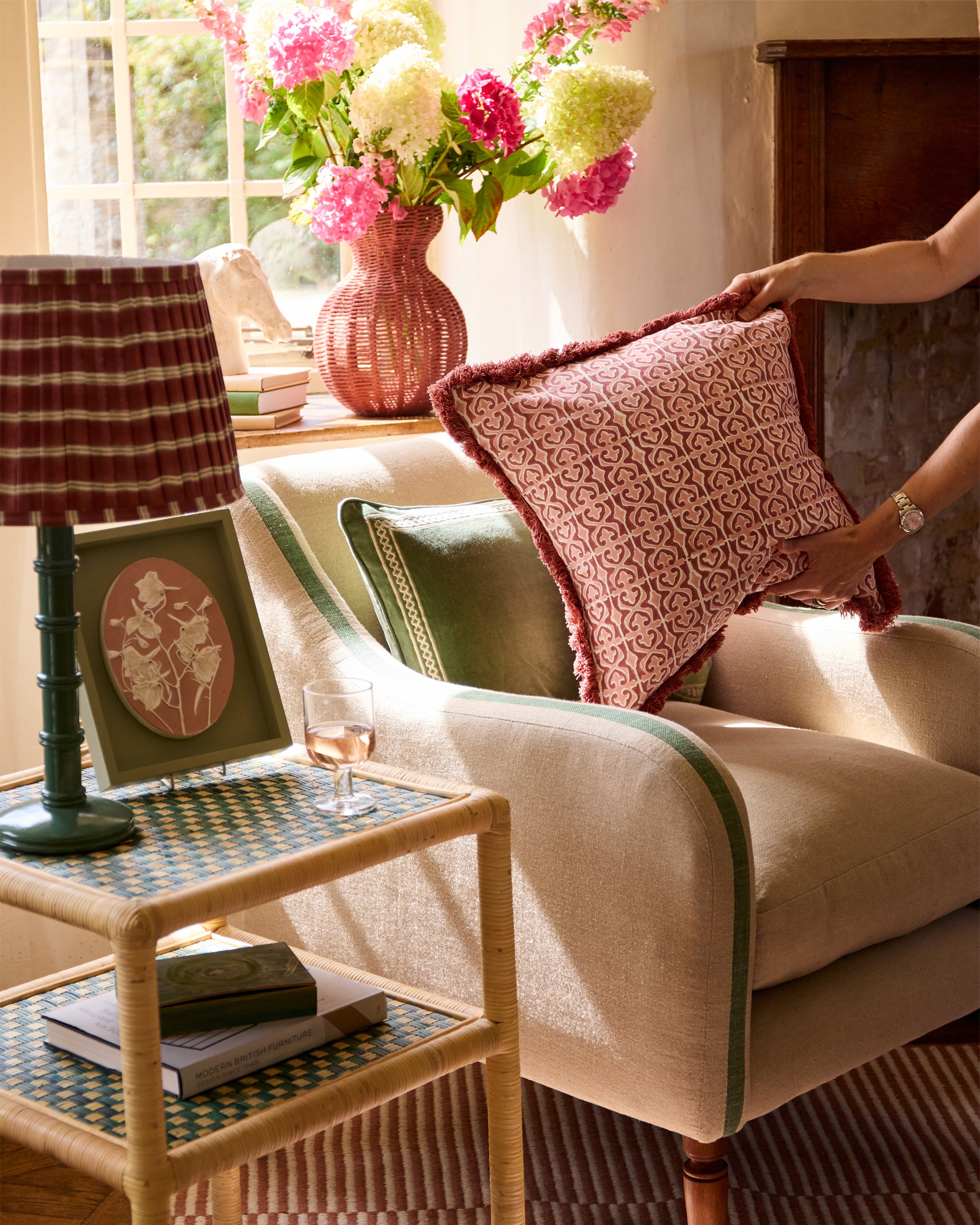 Lifestyle image showing someone placing the pink Santa Clara cushion on the fern upholstered armchair