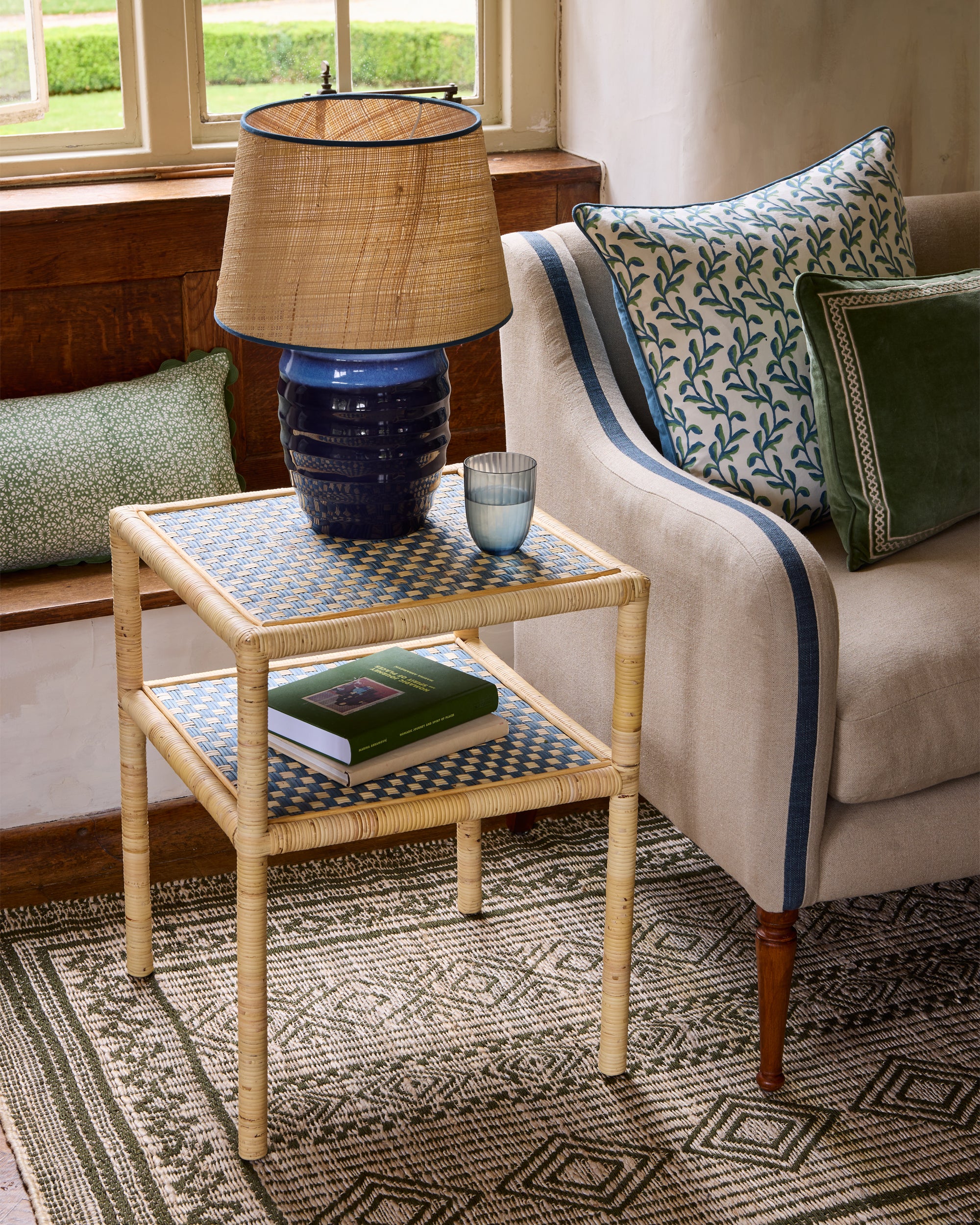 Blue and green sitting room close up lifestyle image showcasing the rattan side table, upholstered sofa and marina square cushion