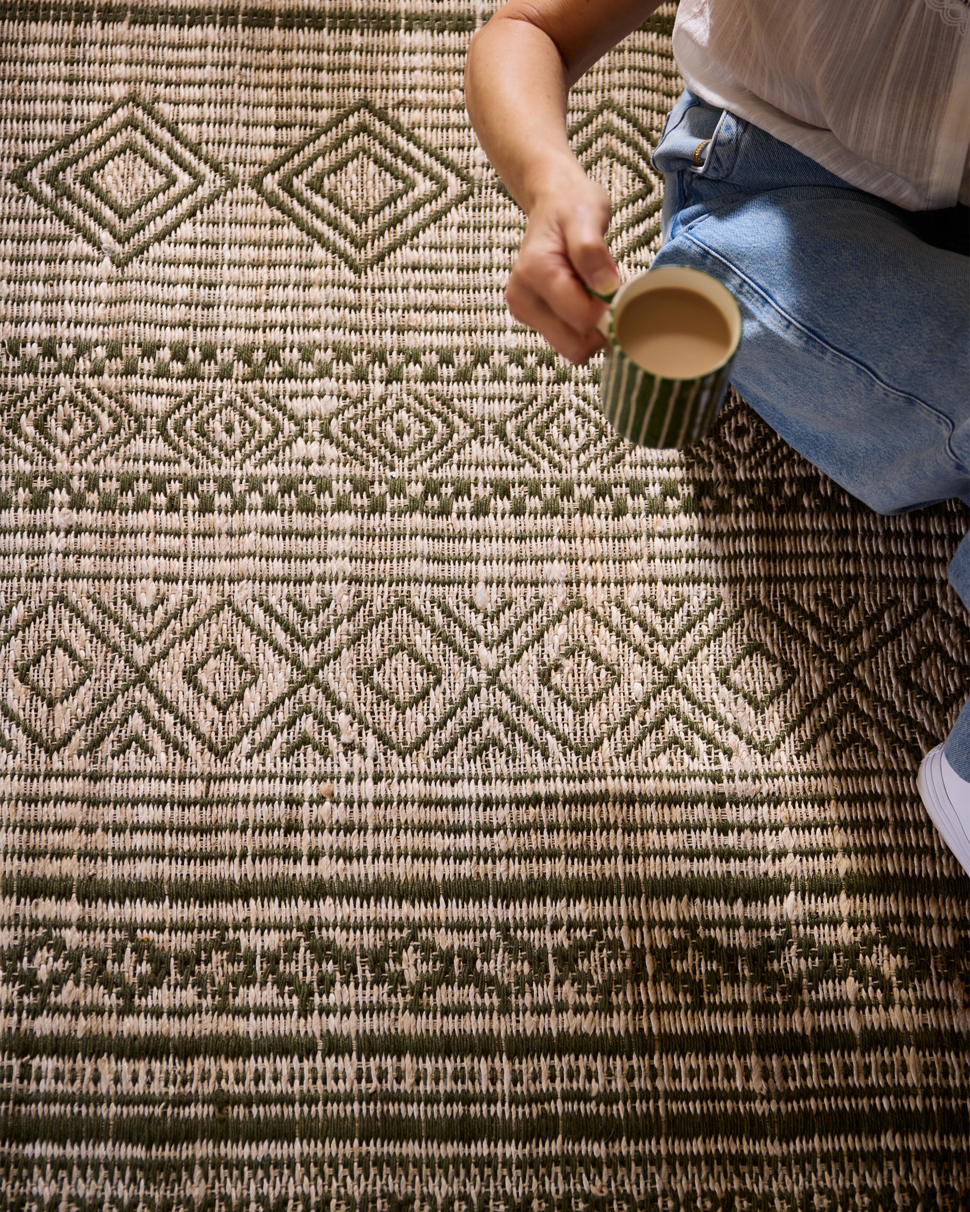 Close up detail lifestyle image of someone sitting on the green moroccan jute rug