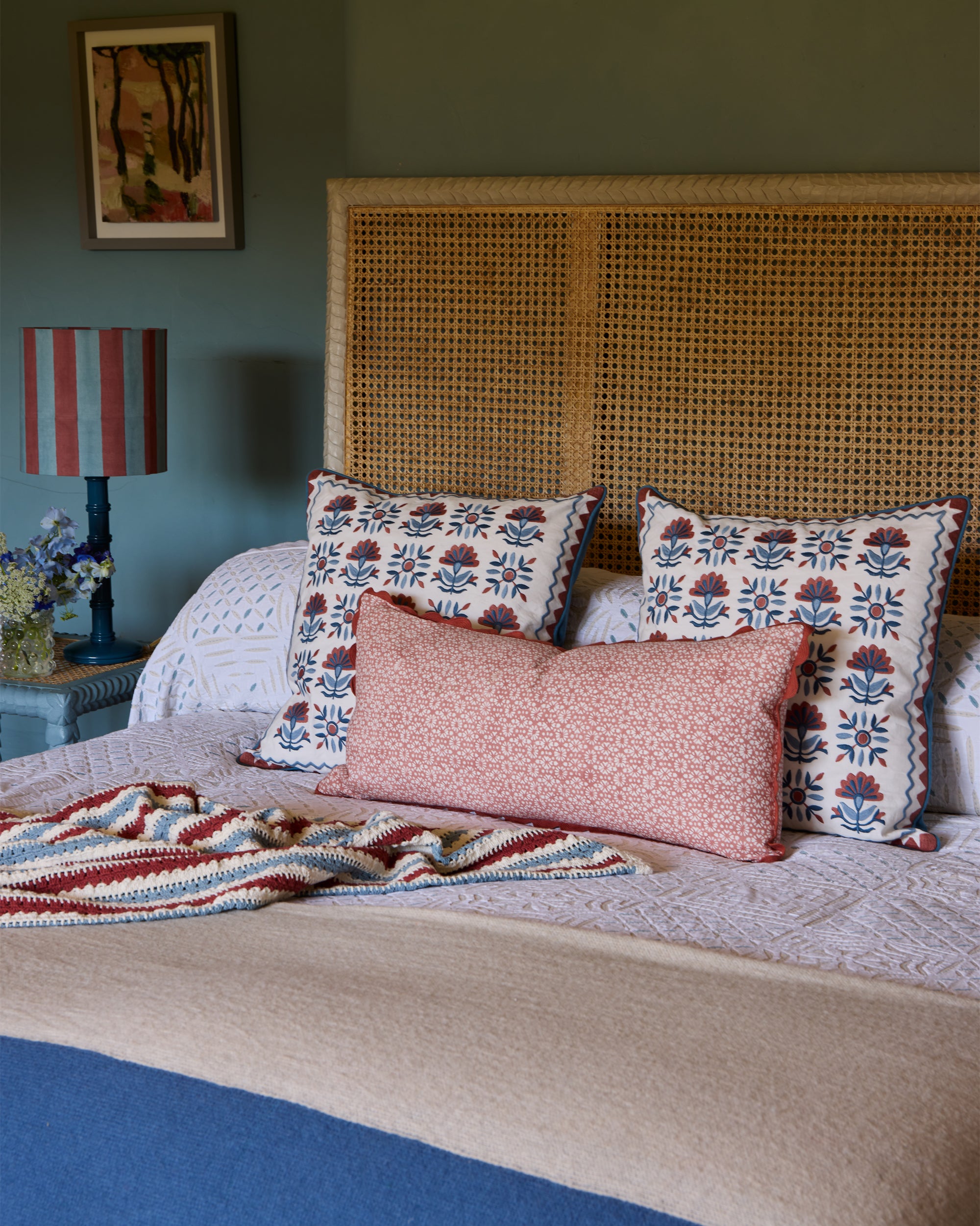 Blue and pink bedroom lifestyle image, featuring the Sancti Embroidered Statement Cushion, Margarita Block Printed Bolster Cushion and Striped Crochet Throw