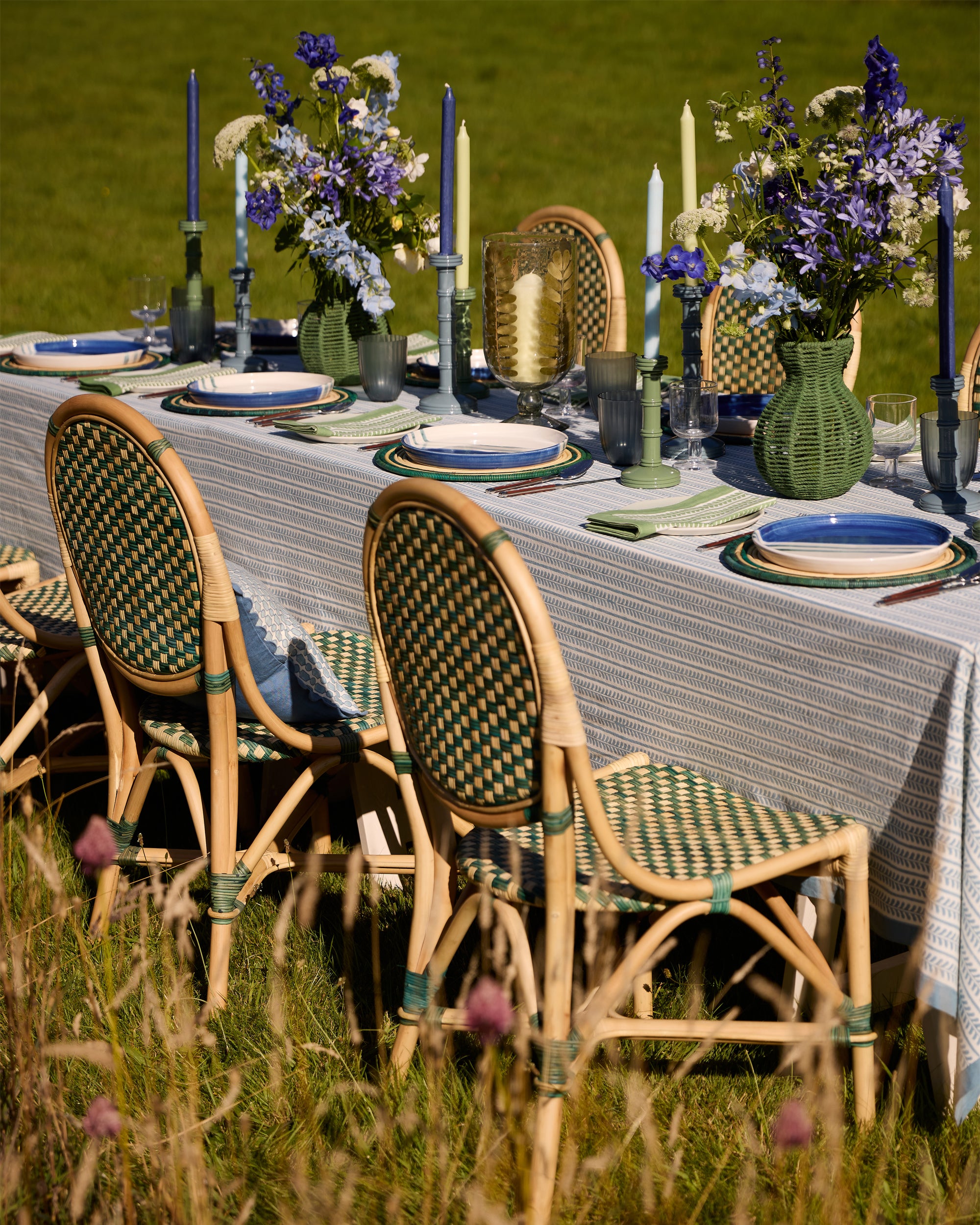 Spring Summer outdoor dining, showcasing the green rattan dining chairs, blue bel tablecloth, green rattan placemats and column candlesticks