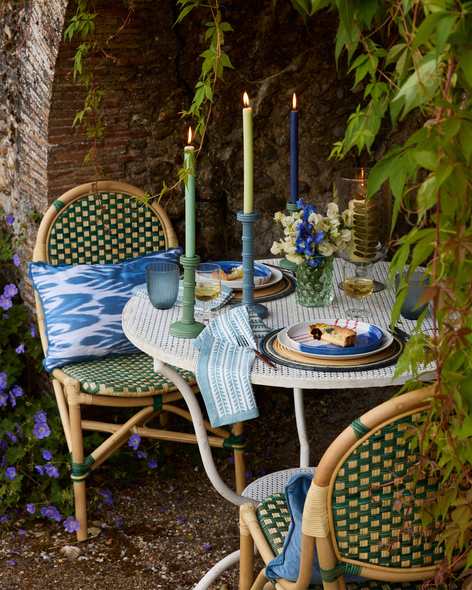 Spring Summer outdoor dining, featuring the green rattan dining chairs, blue ikat cushion, column candlesticks and rattan placemats