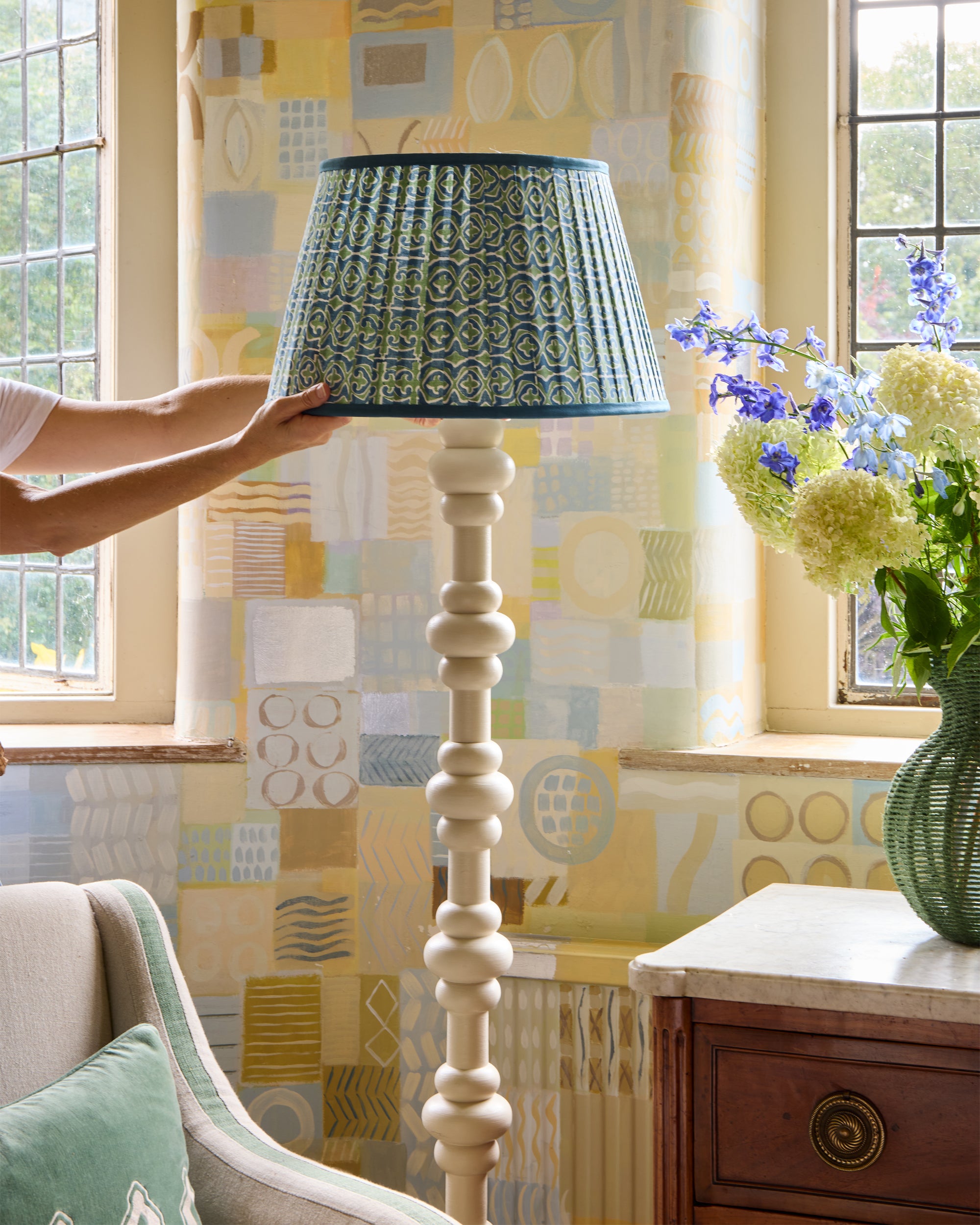 Lifestyle image showing someone placing the blue and green Santa Clara pleated lampshade on the taupe abacus floor lamp