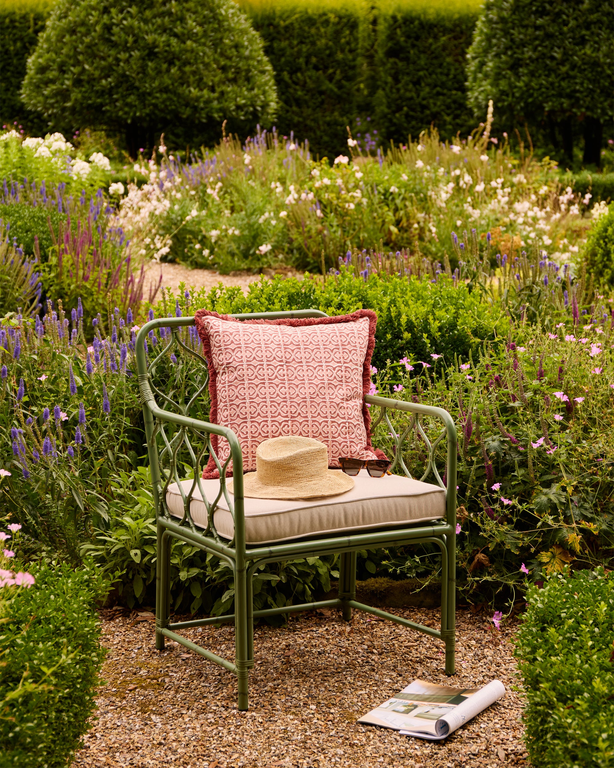 Green Curato armchair with a pink cushion and straw hat in a garden setting