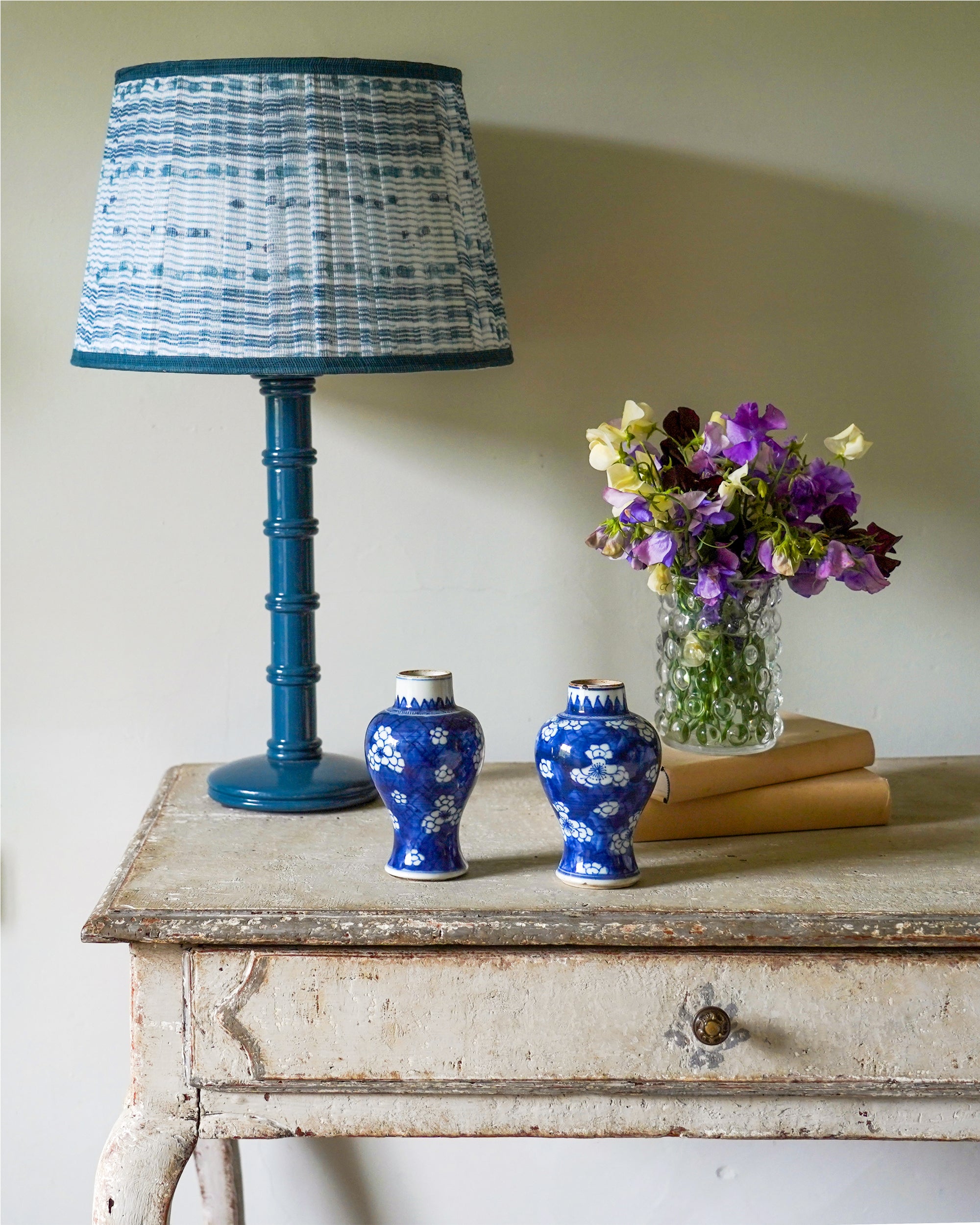 Blue lamp with patterned blue shade on a wooden table with decorative vases and flowers.