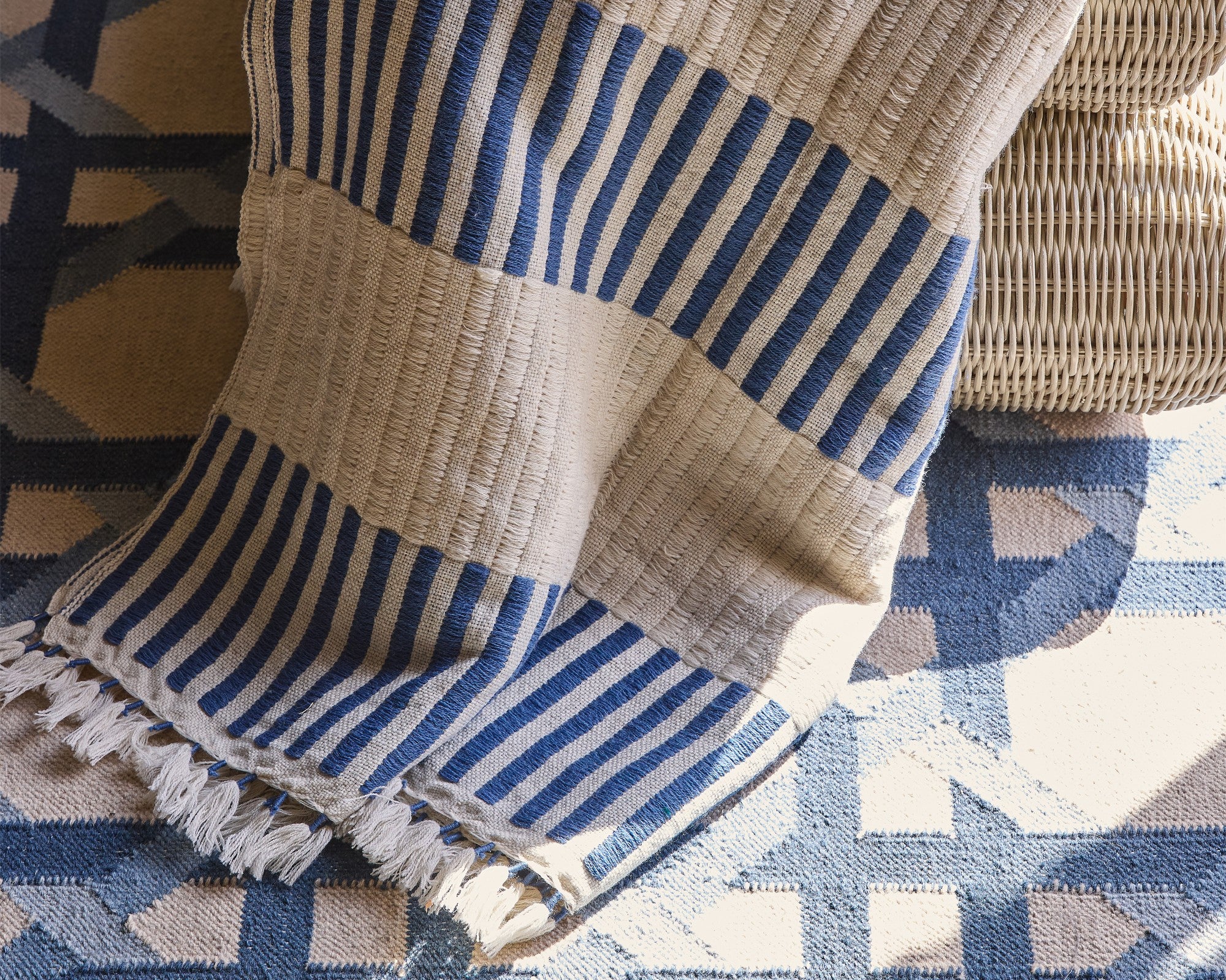 Striped blue and beige blanket with fringe on a patterned surface