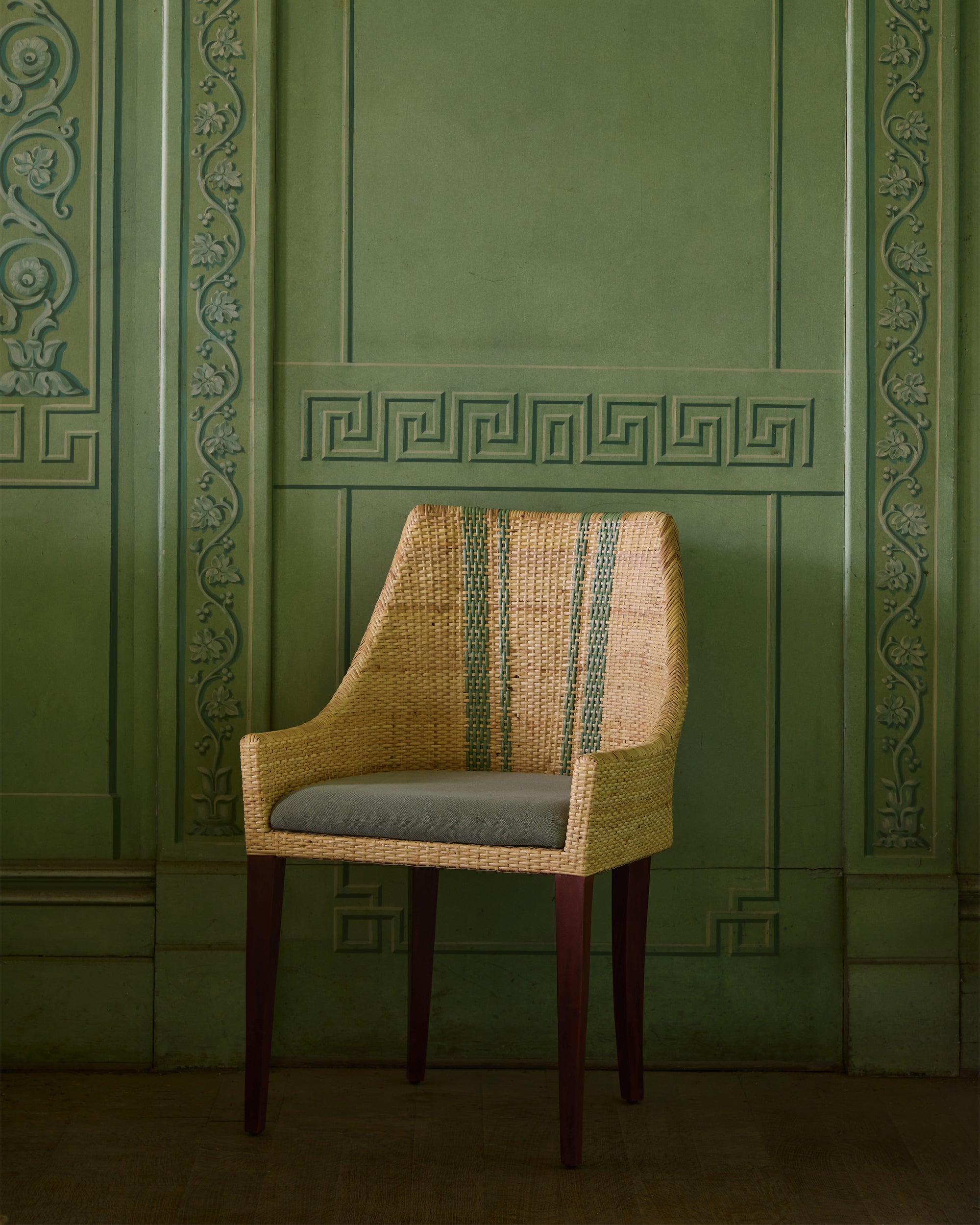 Woven chair with a green cushion against a green panelled wall