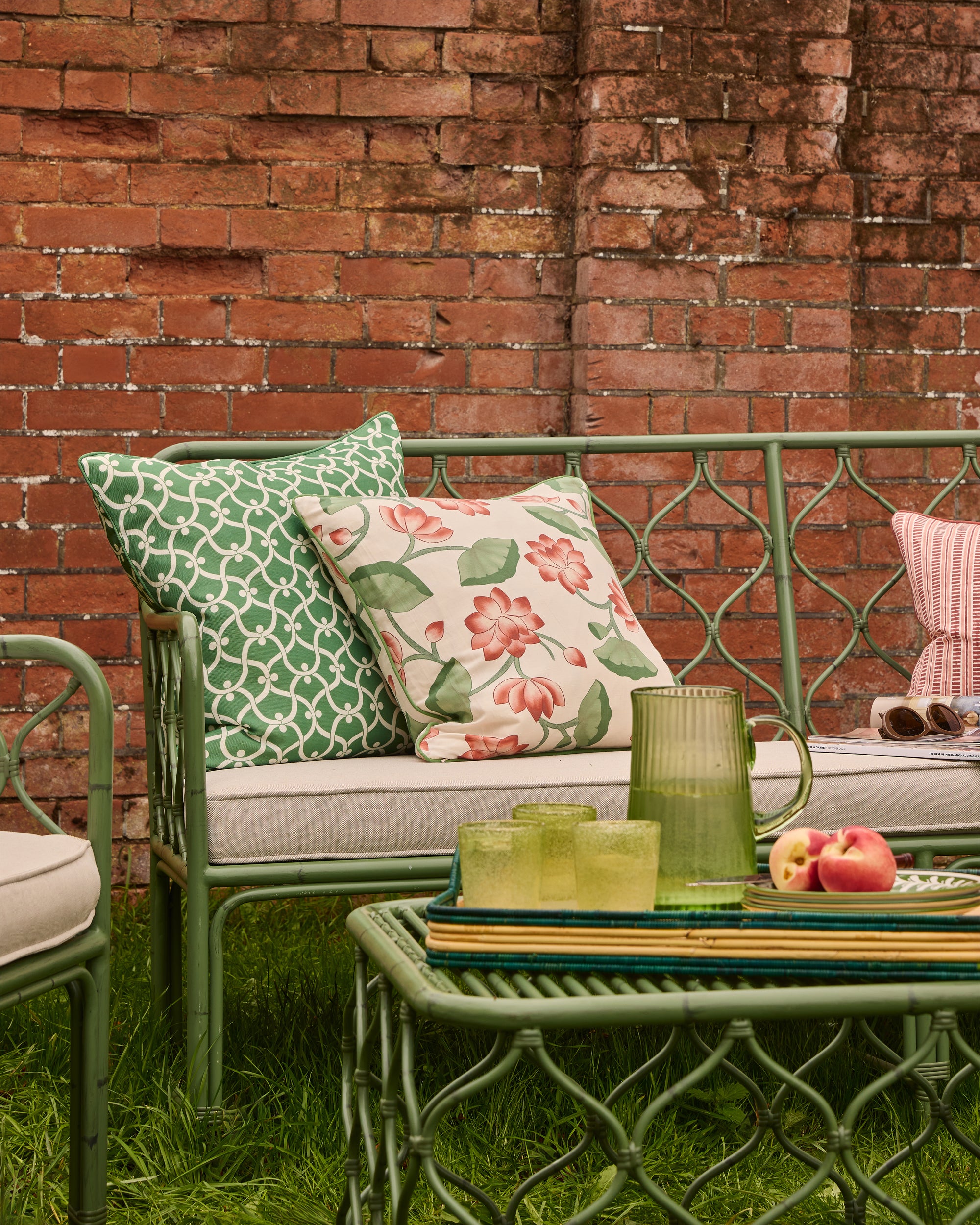 Outdoor seating area with green metal furniture, cushions, and a brick wall background.