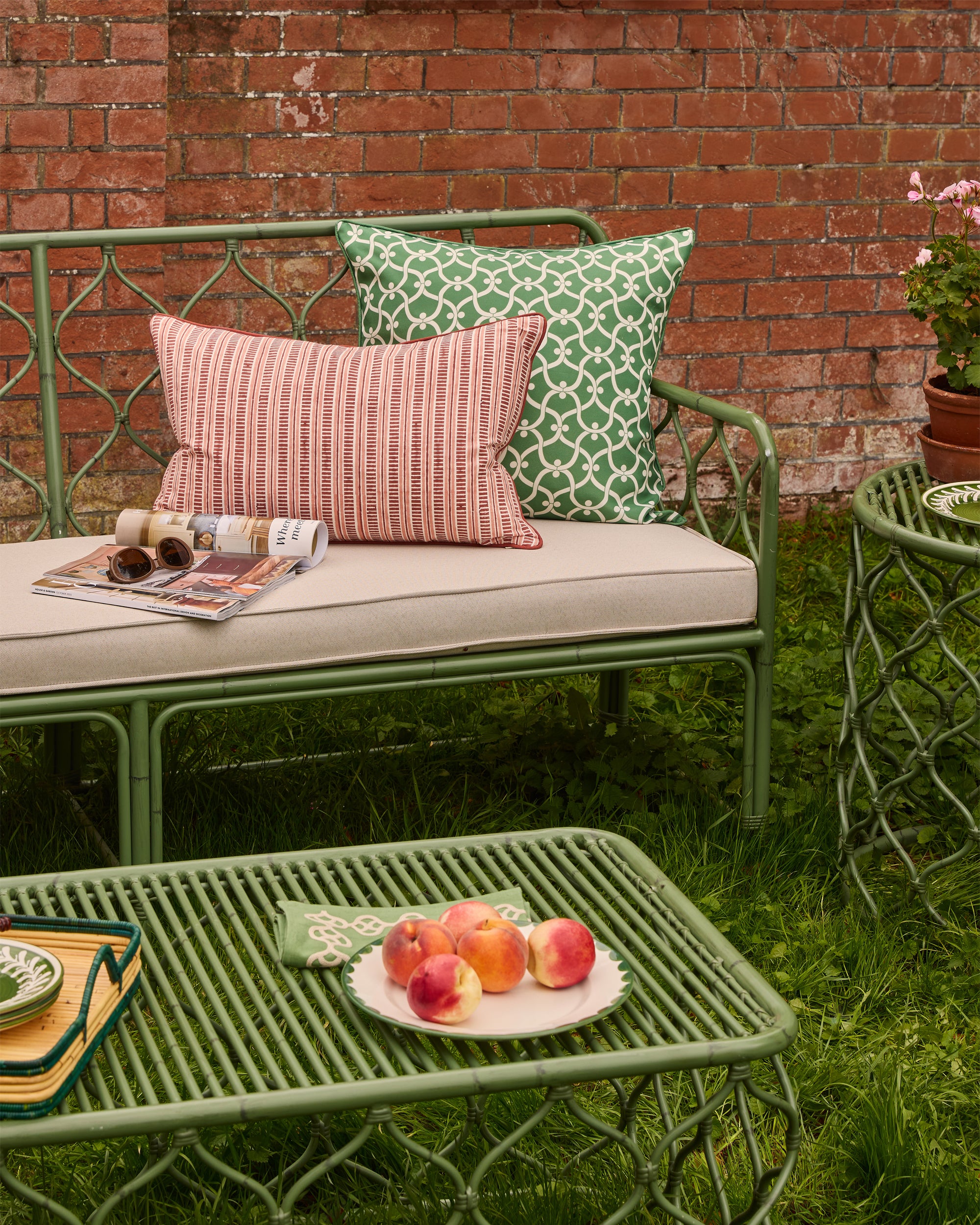 Outdoor seating area with a green bench and table against a brick wall.
