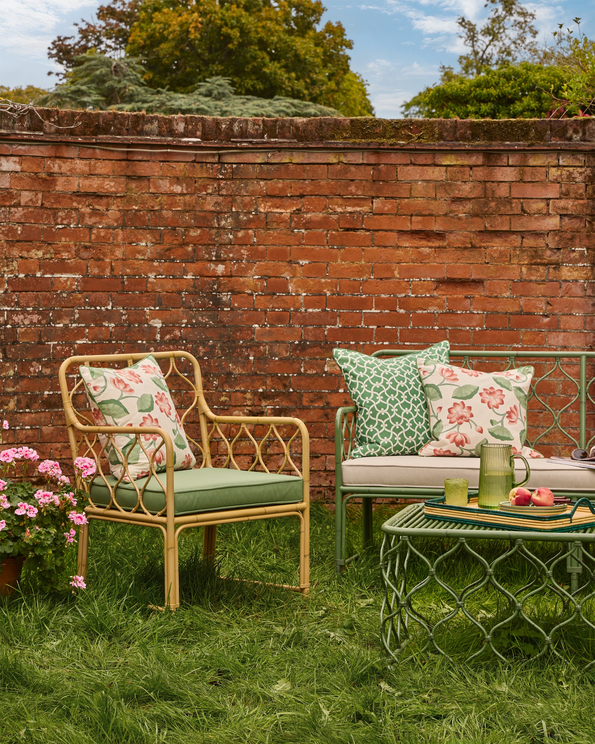 Outdoor garden setting with wicker chairs, cushions, and a small table against a brick wall.