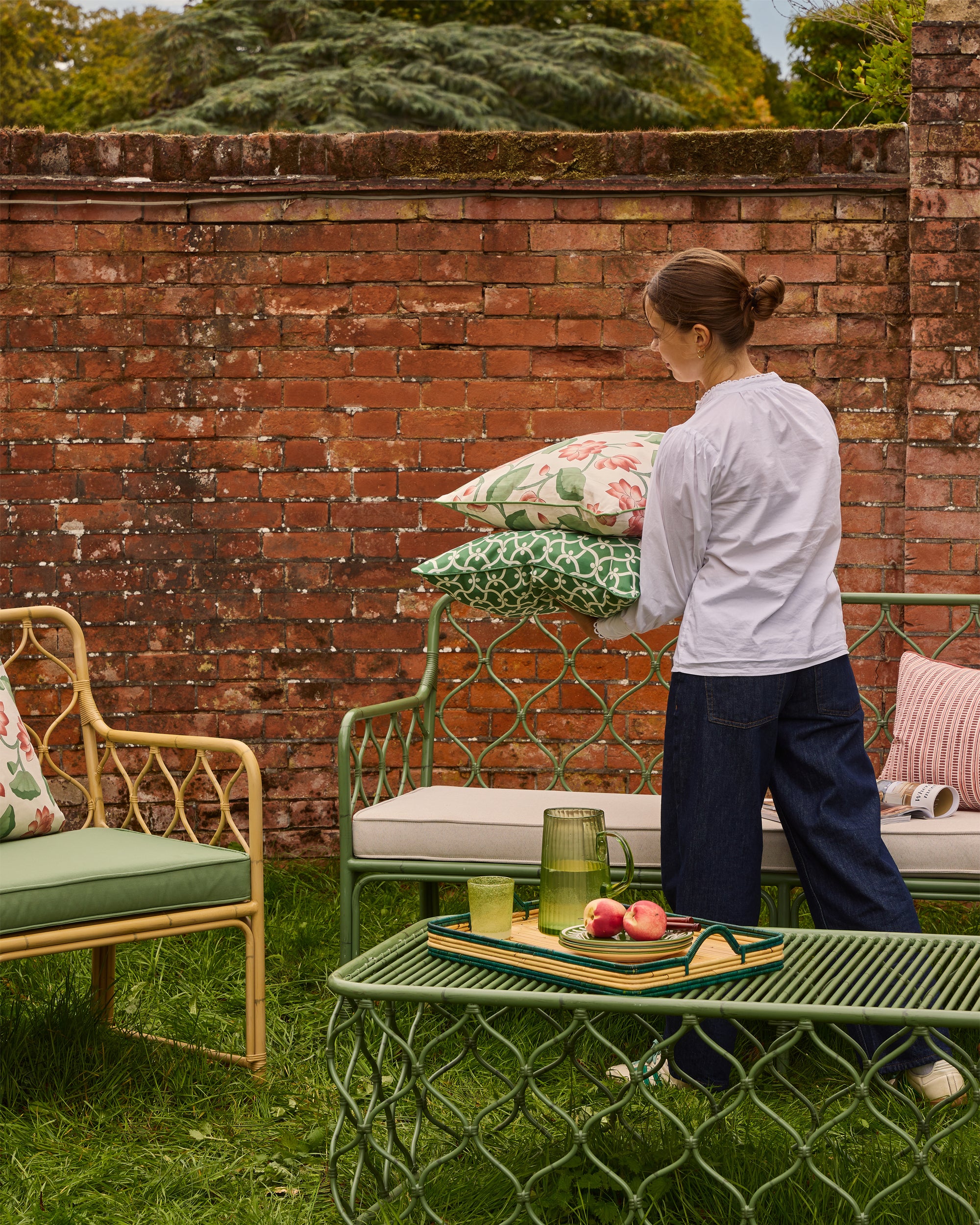 Woman arranging cushions on outdoor furniture in a garden setting.