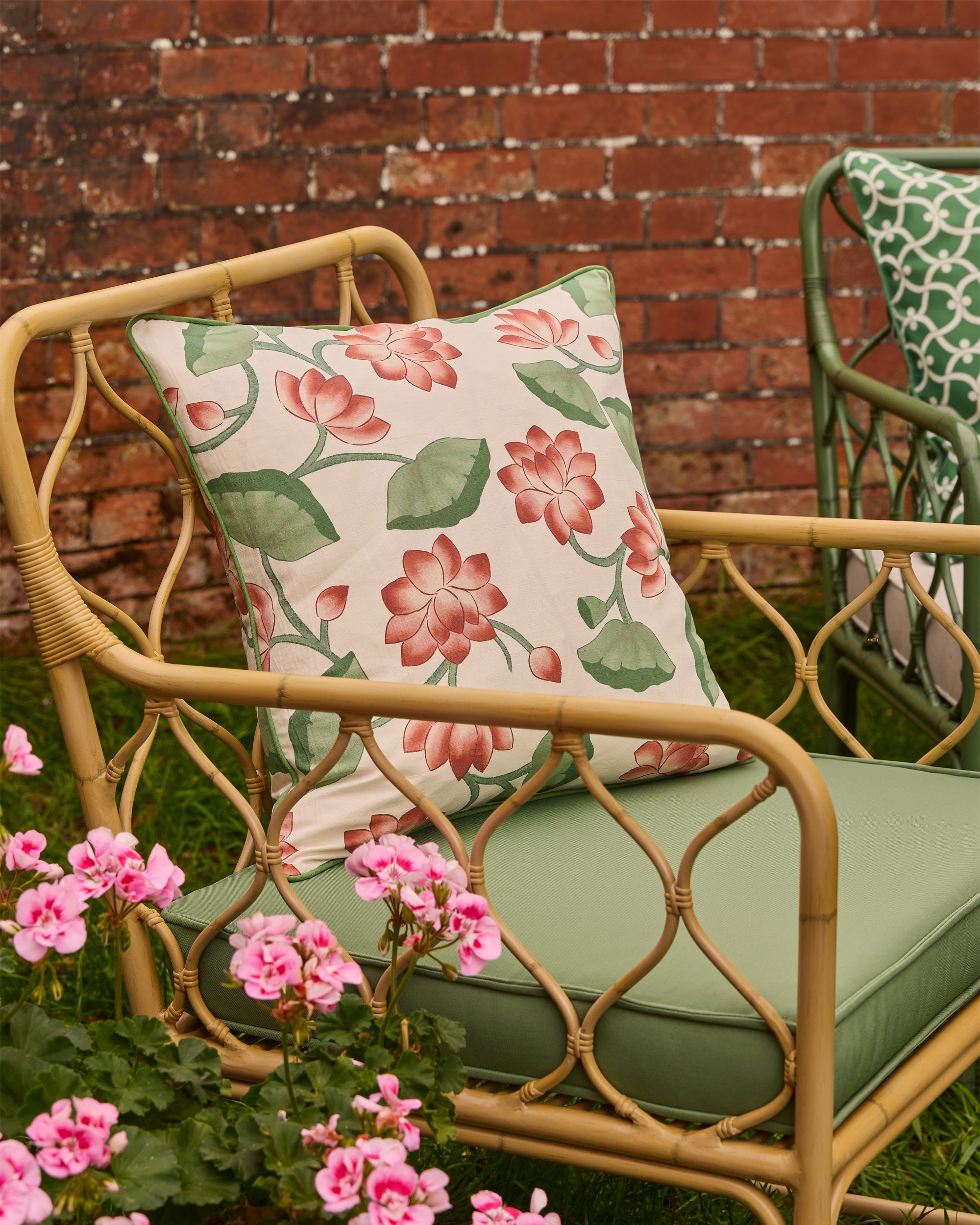 Decorative pillow with floral pattern on a wicker chair with green cushion, against a brick wall.