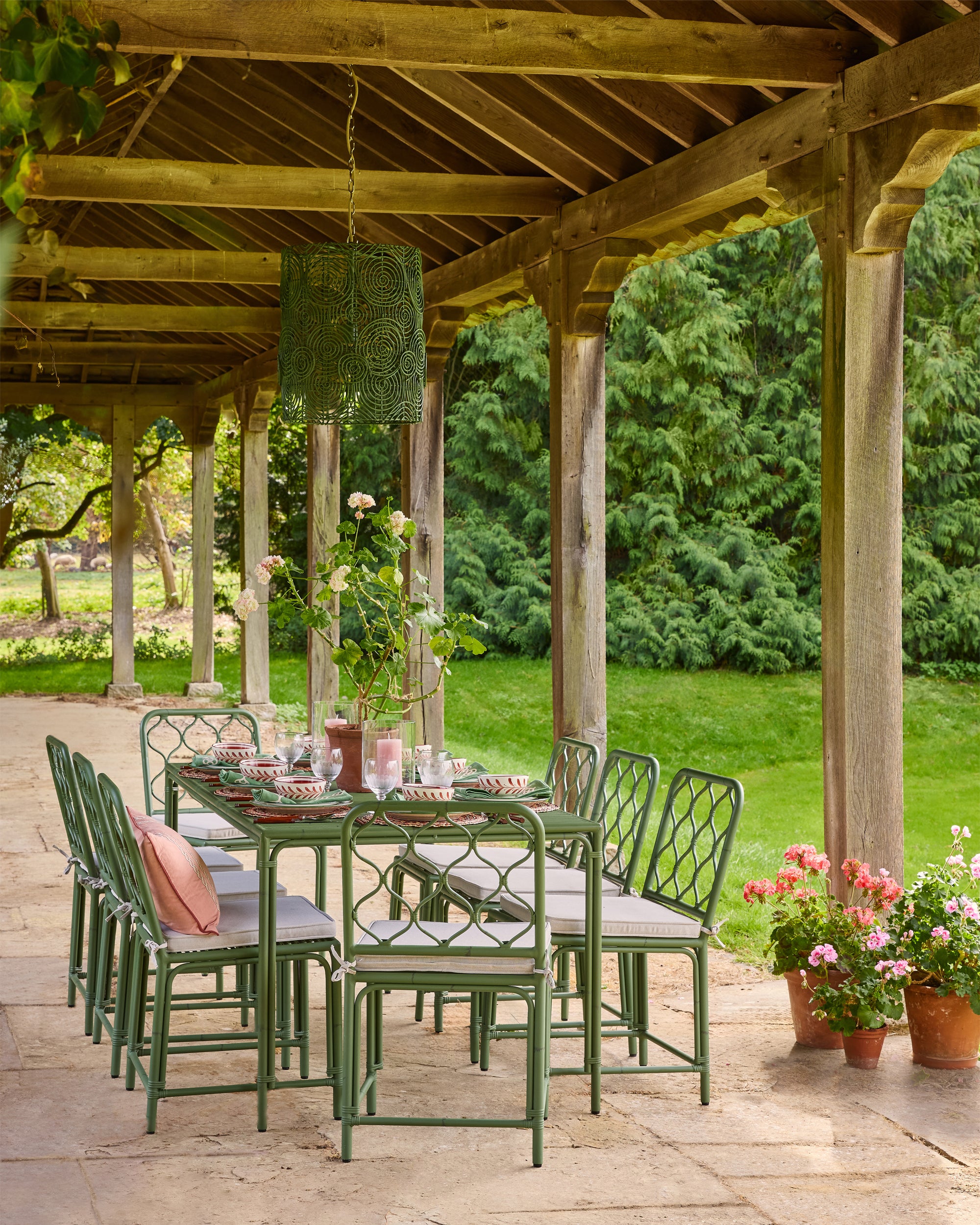 Outdoor dining setup under a wooden pergola with green chairs and table, surrounded by greenery.