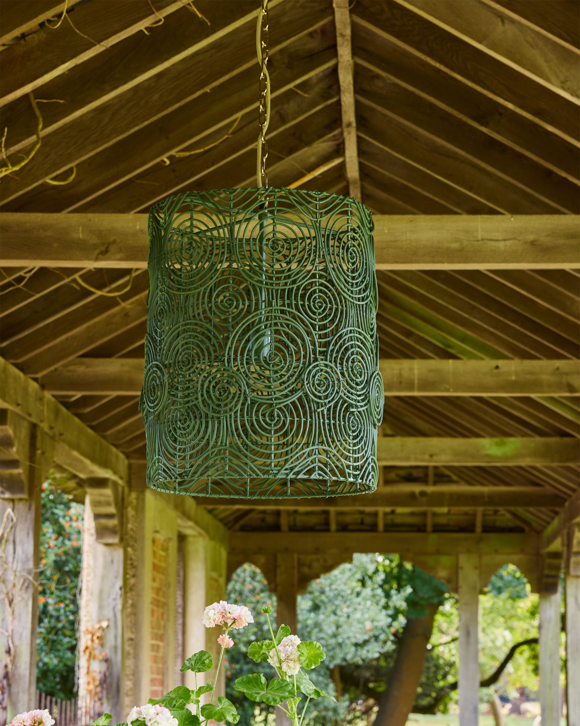 Decorative green lamp hanging from a wooden ceiling with a garden view in the background
