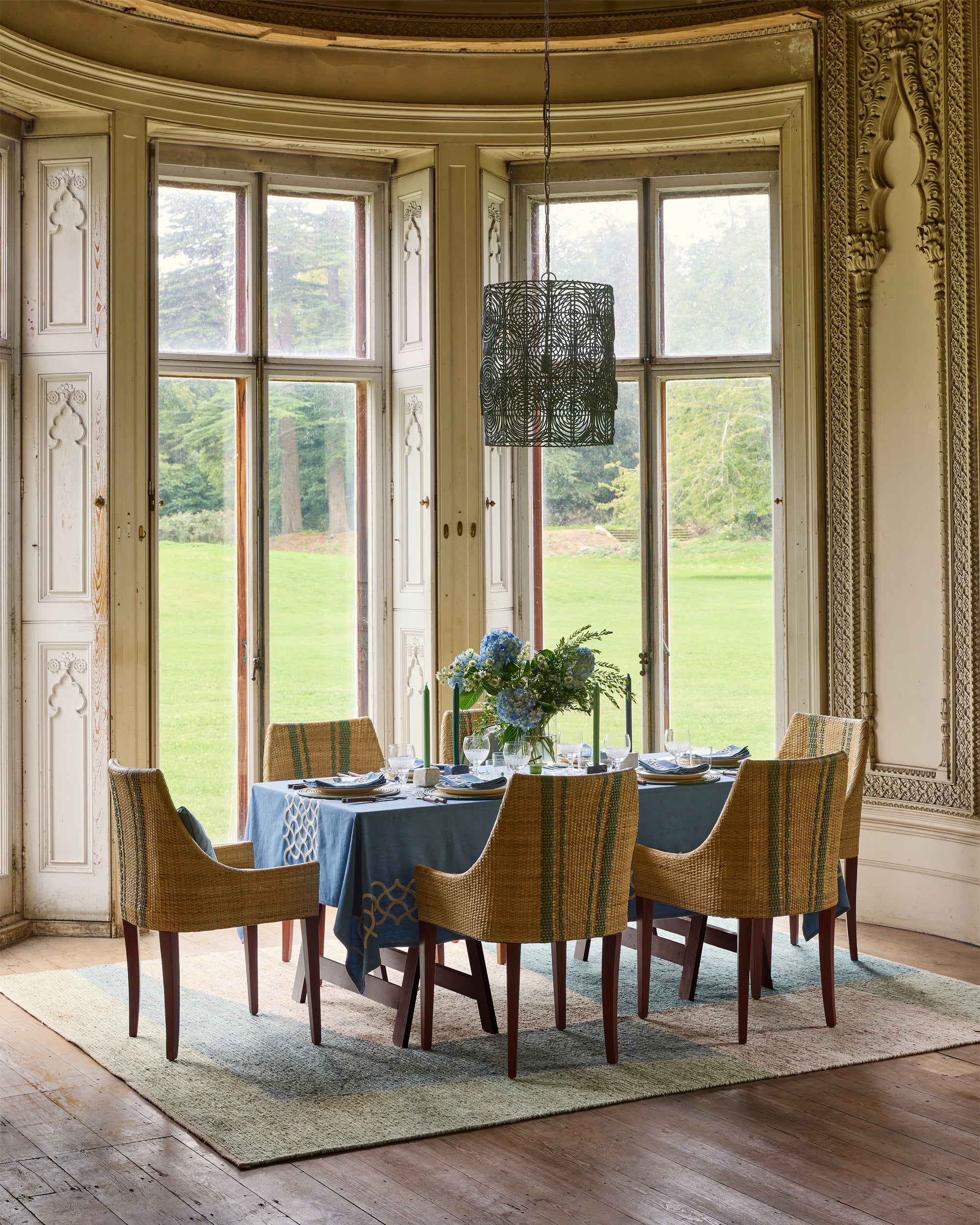 Dining room with large windows, wooden chairs, and a table set for a meal.