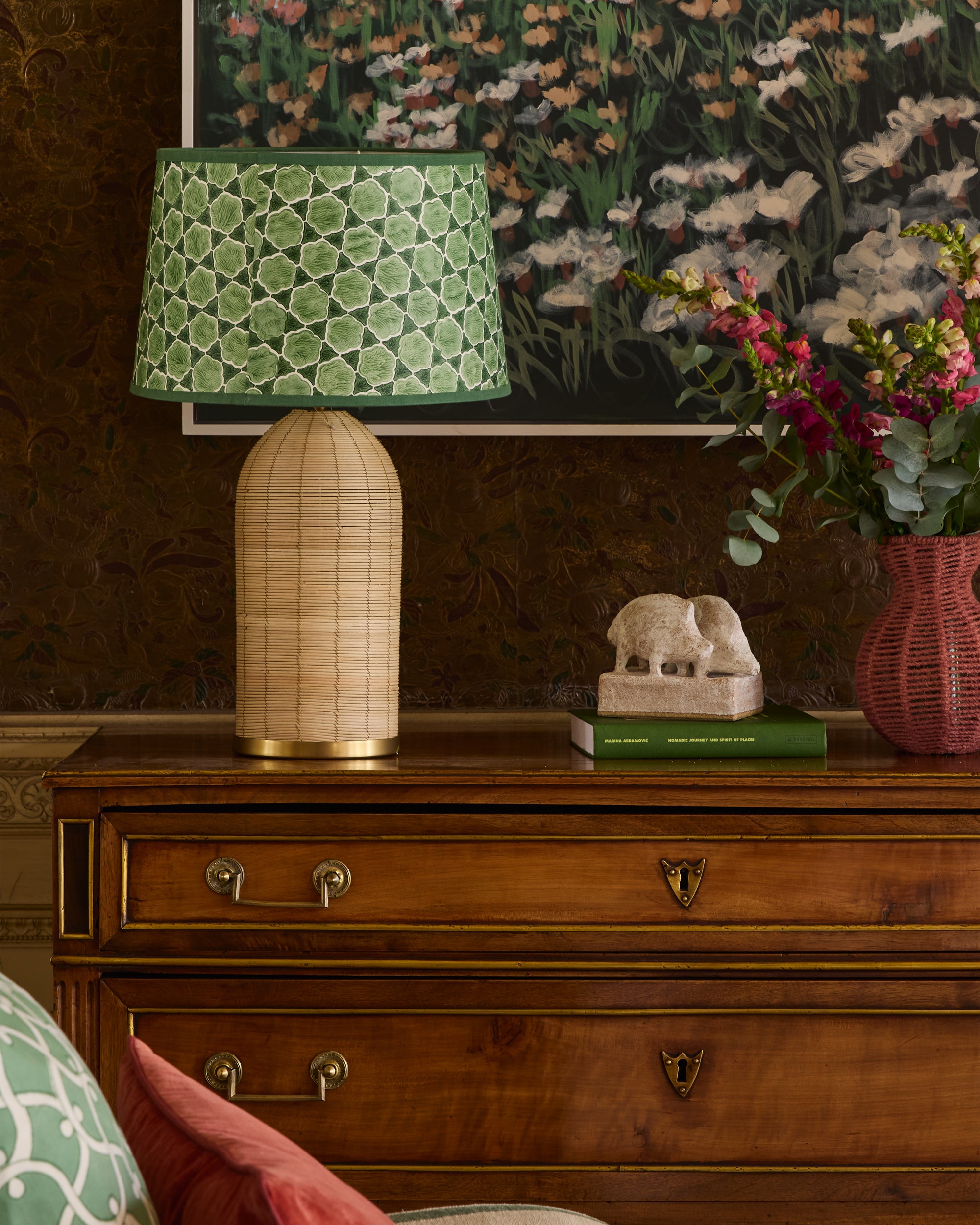 Decorative lamp with green patterned shade on a wooden dresser with books and a vase.