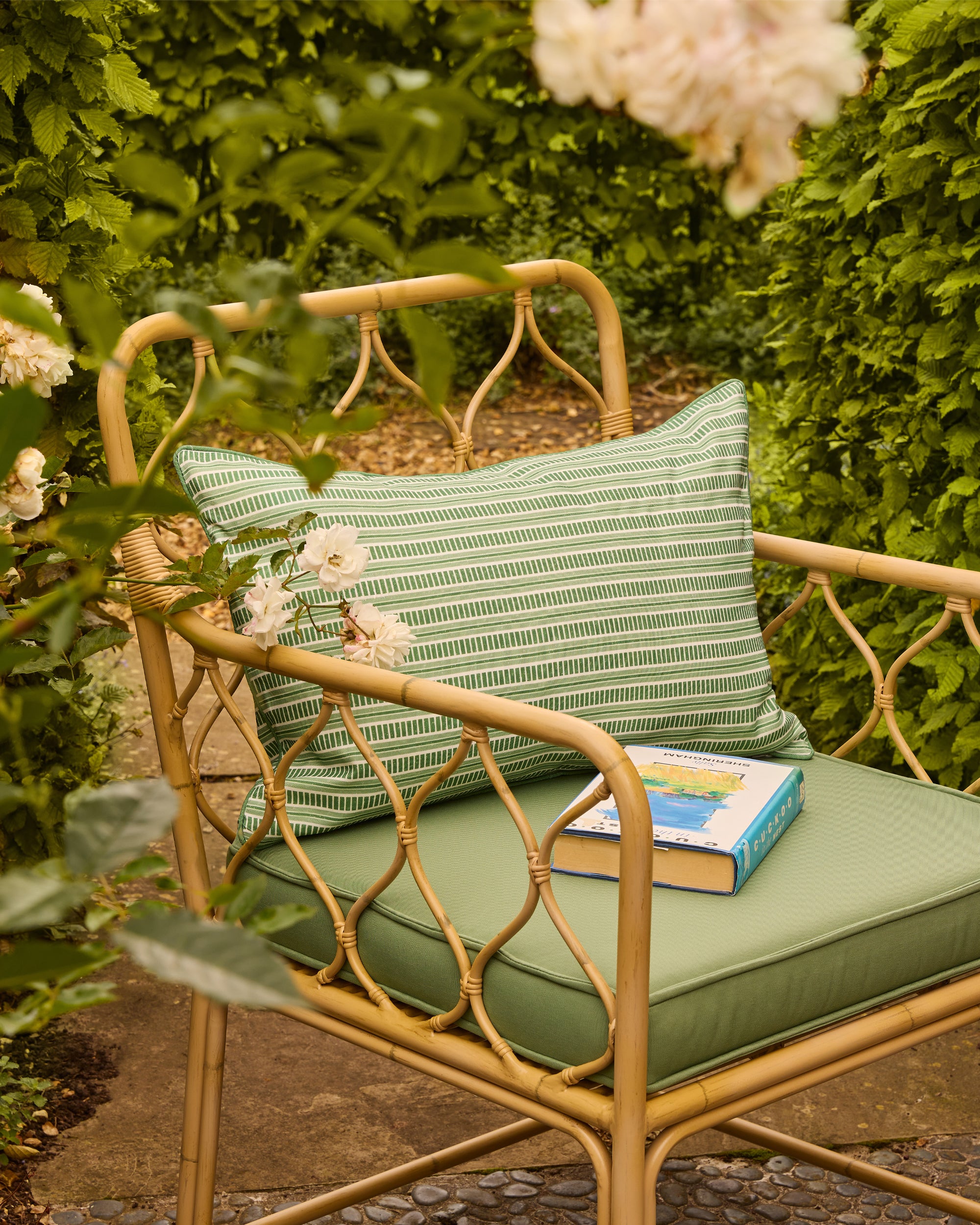 Rattan bench with green cushions and a book, surrounded by greenery