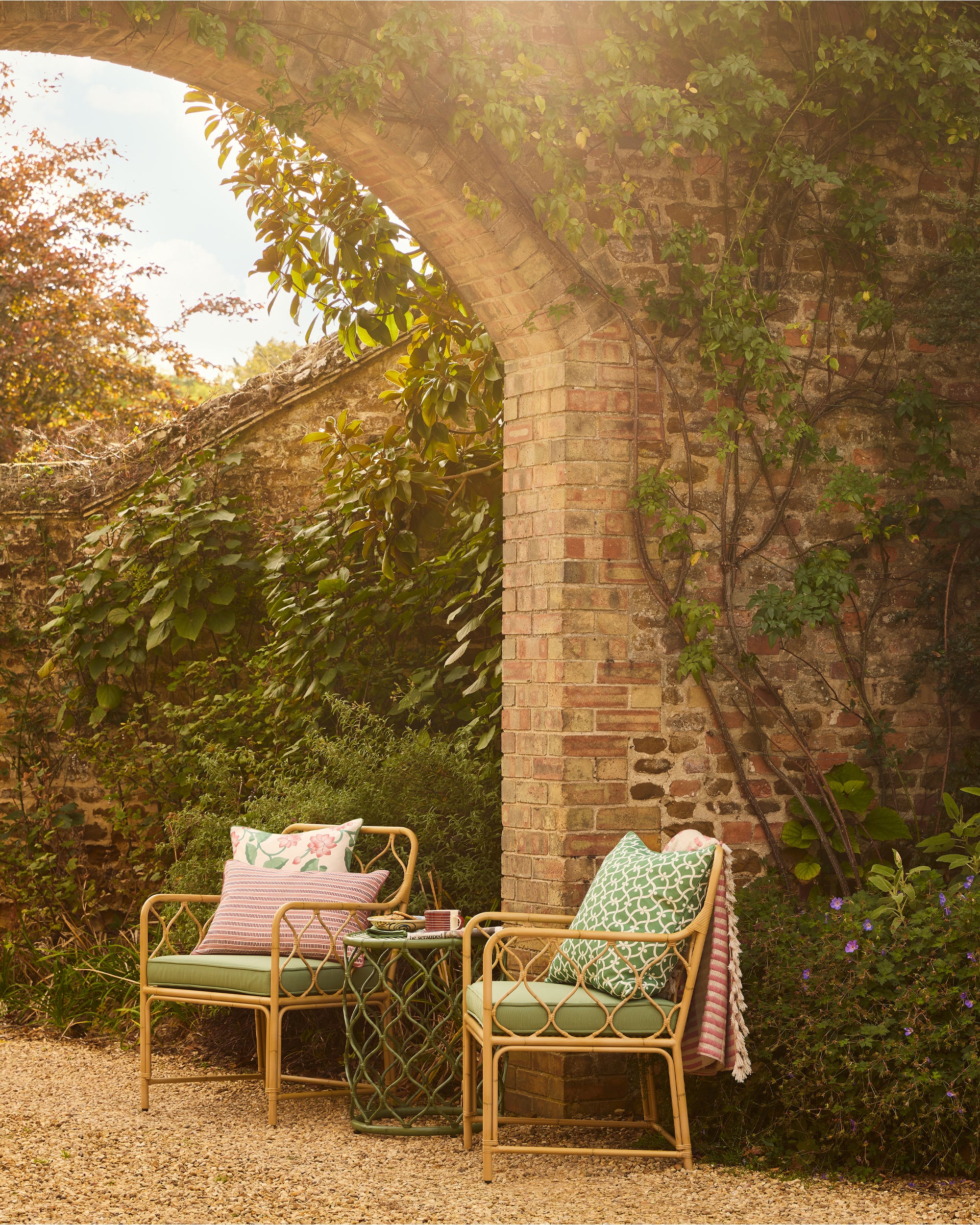 Outdoor seating area with two chairs and a small table against a brick wall and greenery.