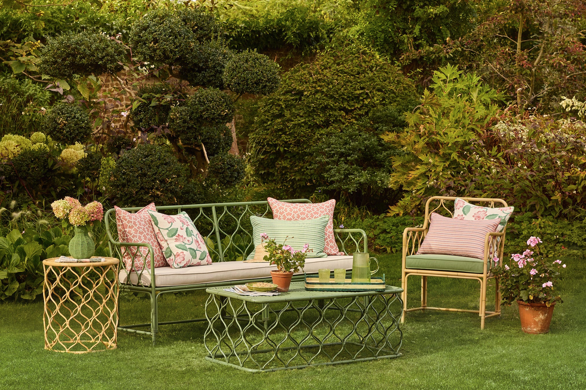 Outdoor garden setting with a green sofa, armchair, and coffee table surrounded by plants.